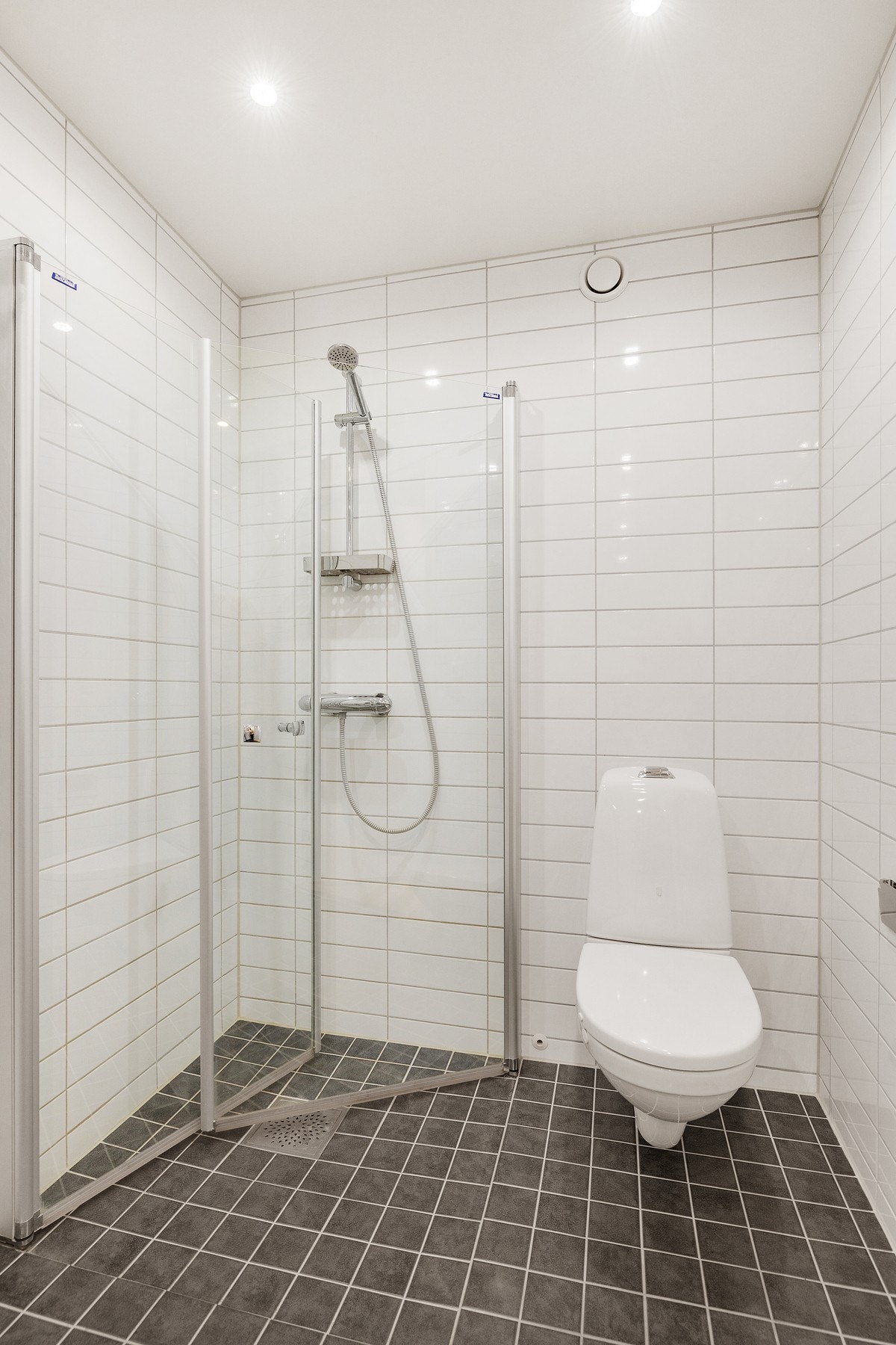 Et lyst og lekkert bad med eget dusjhjørne, vegghengt toalett og servant med over -og underskap. Galleribilde