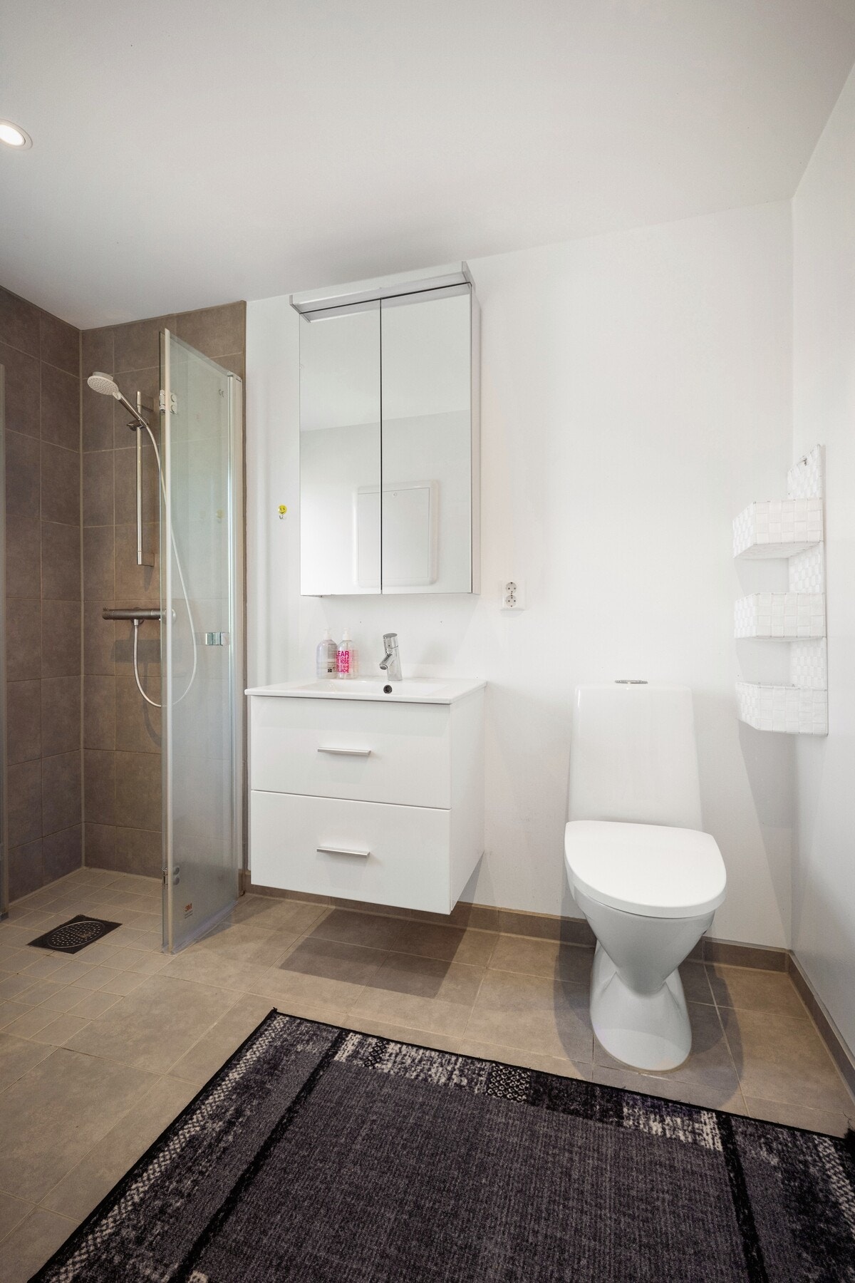 Hovedbadet er moderne. Her det lyse og grå overflater og gulvvarme, dusjhjørne med glassdører, gulvstående toalett og en lys baderomsinnredning med servant og speilskap med belysning. Galleribilde
