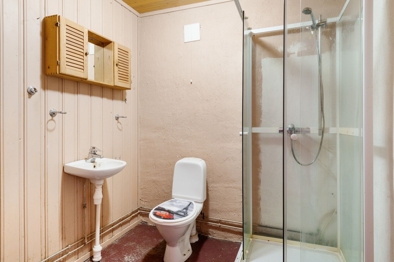 Sanitærrom innredet med servant, dusjkabinett og gulvmontert toalett. Flatene er dekket med betonggulv, murpuss og panel på vegger, og panel i himling. Galleribilde