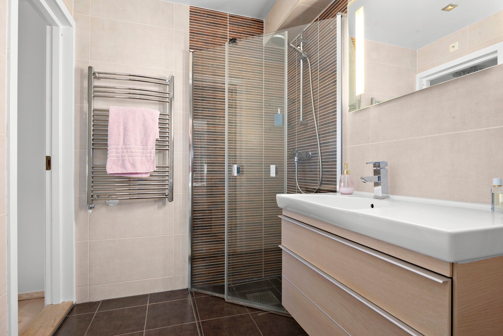 Rommet er innredet med servantinnredning med skuffer, vegghengt skap med speilfront, dusjhjørne med glassdører og gulvstående toalett Galleribilde