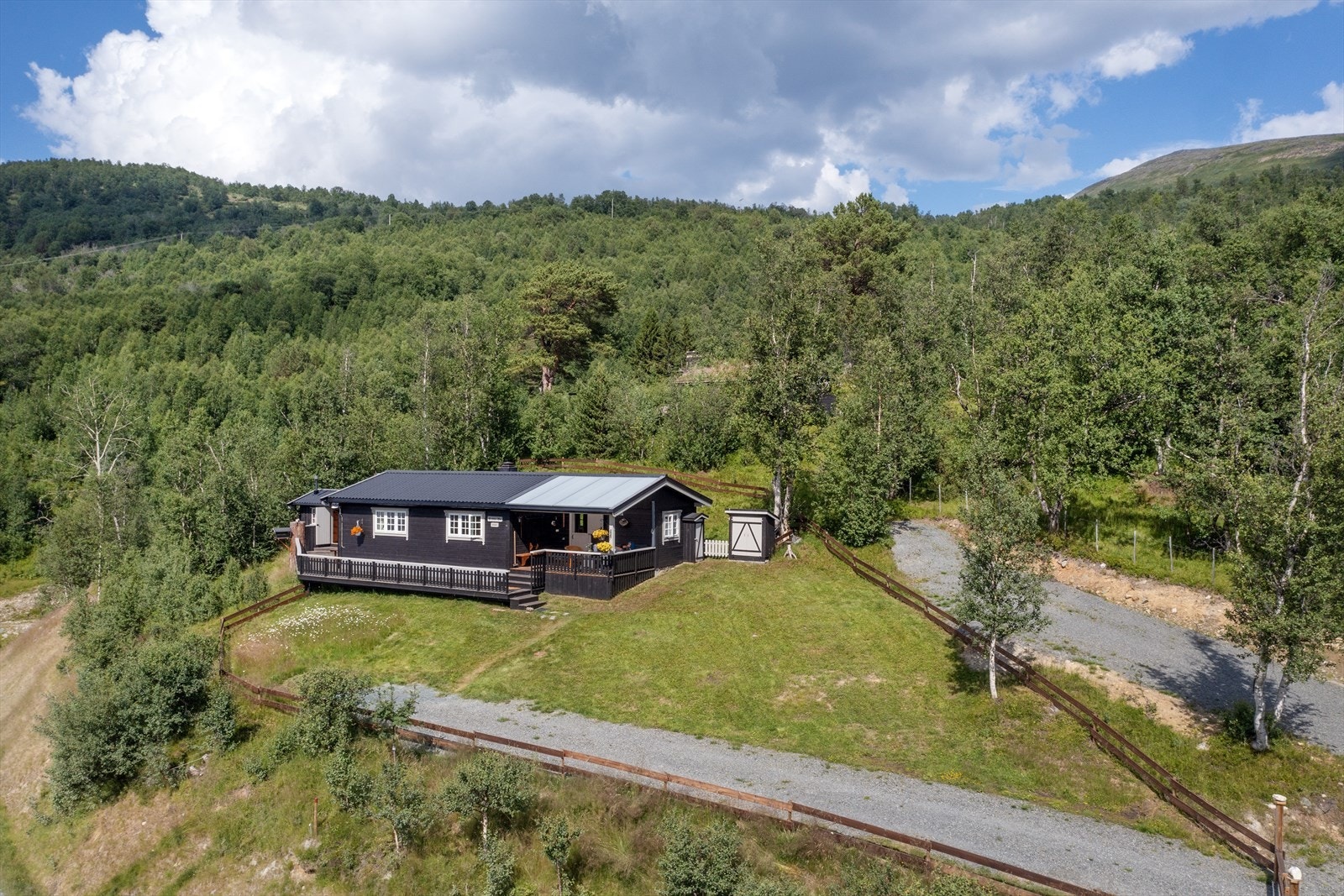 Tomten består av naturtomt, gressbakke/plen og gruset innkjørsel, og er delvis innrammet av lavt plankgjerde med grind Galleribilde