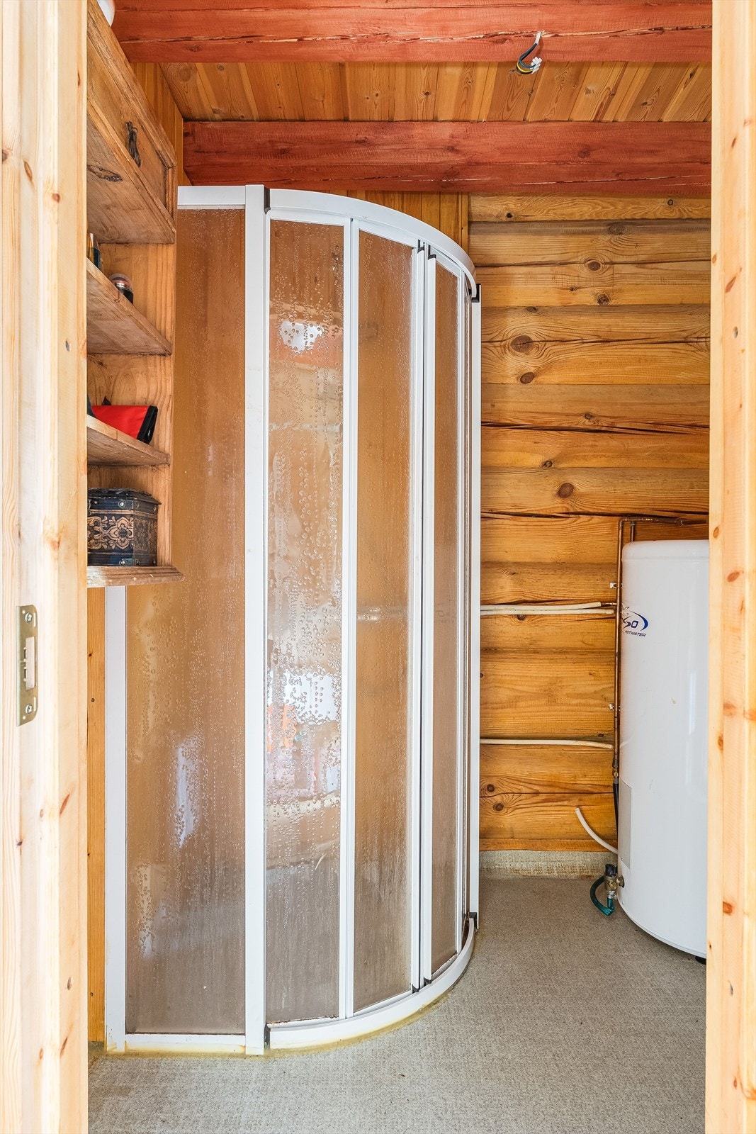 Bod innredet som et baderom med våtromsbelegg på gulv, overflater med panel og tømmer, samt elektrisk styrt vifte. Rommet er utstyrt med dusjhjørne med vegghengt dusj, skyllekar og varmtvannsbereder. Galleribilde