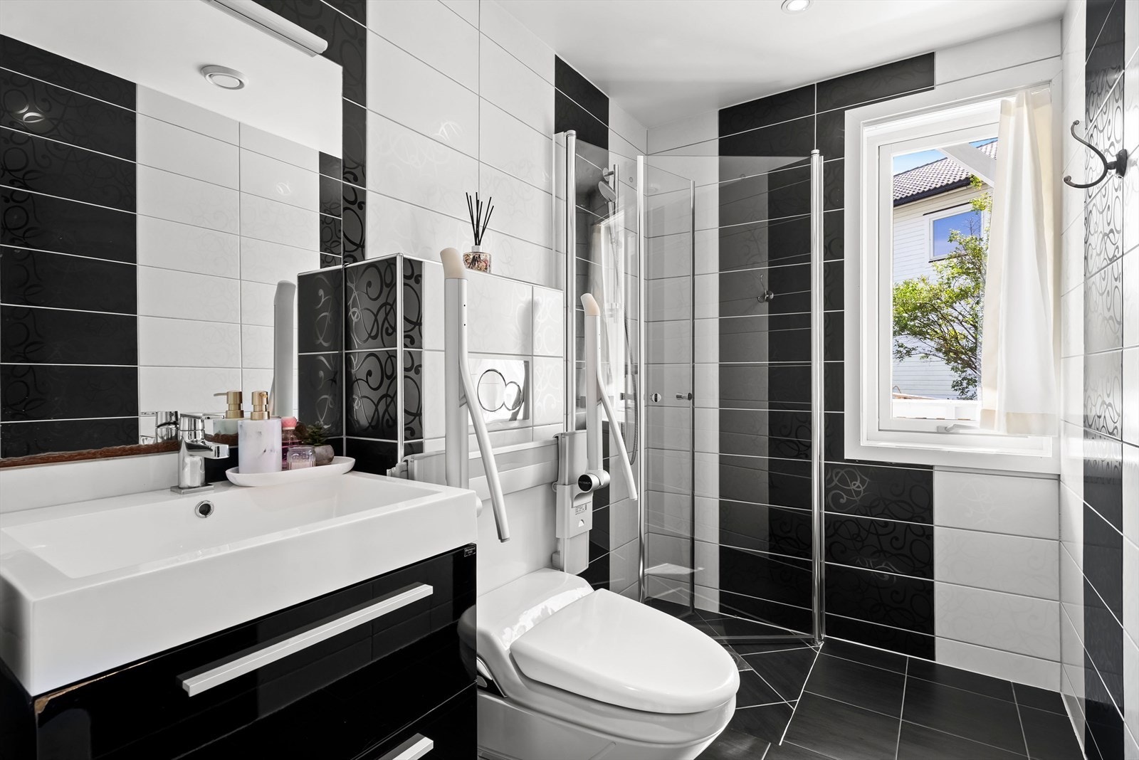 Helfliset bad med dusj på gulv med dører i herdet glass, servant og veggfestet klosett med innebygget sisterne Galleribilde