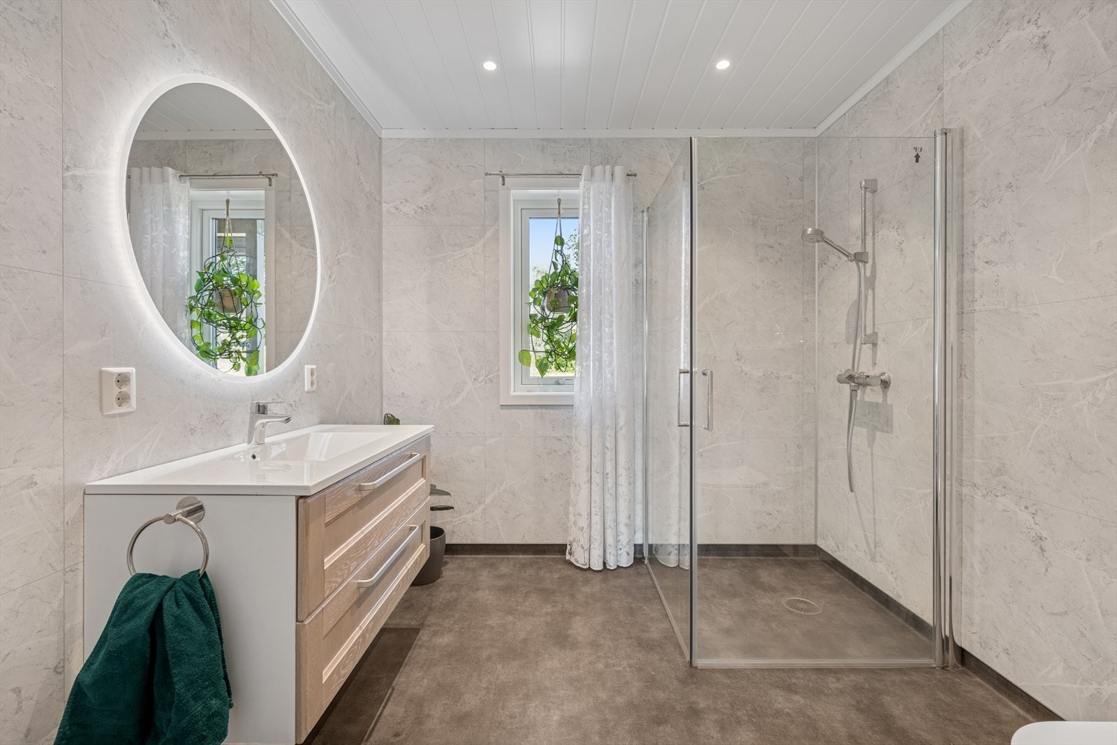 Badet har vinylbelegg på gulv med behagelig gulvvarme og vegger har baderomsplater. Av utstyr er det skuffeinnredning med overliggende servant, dusjhørne med innfellbare dusjdører og toalett Galleribilde