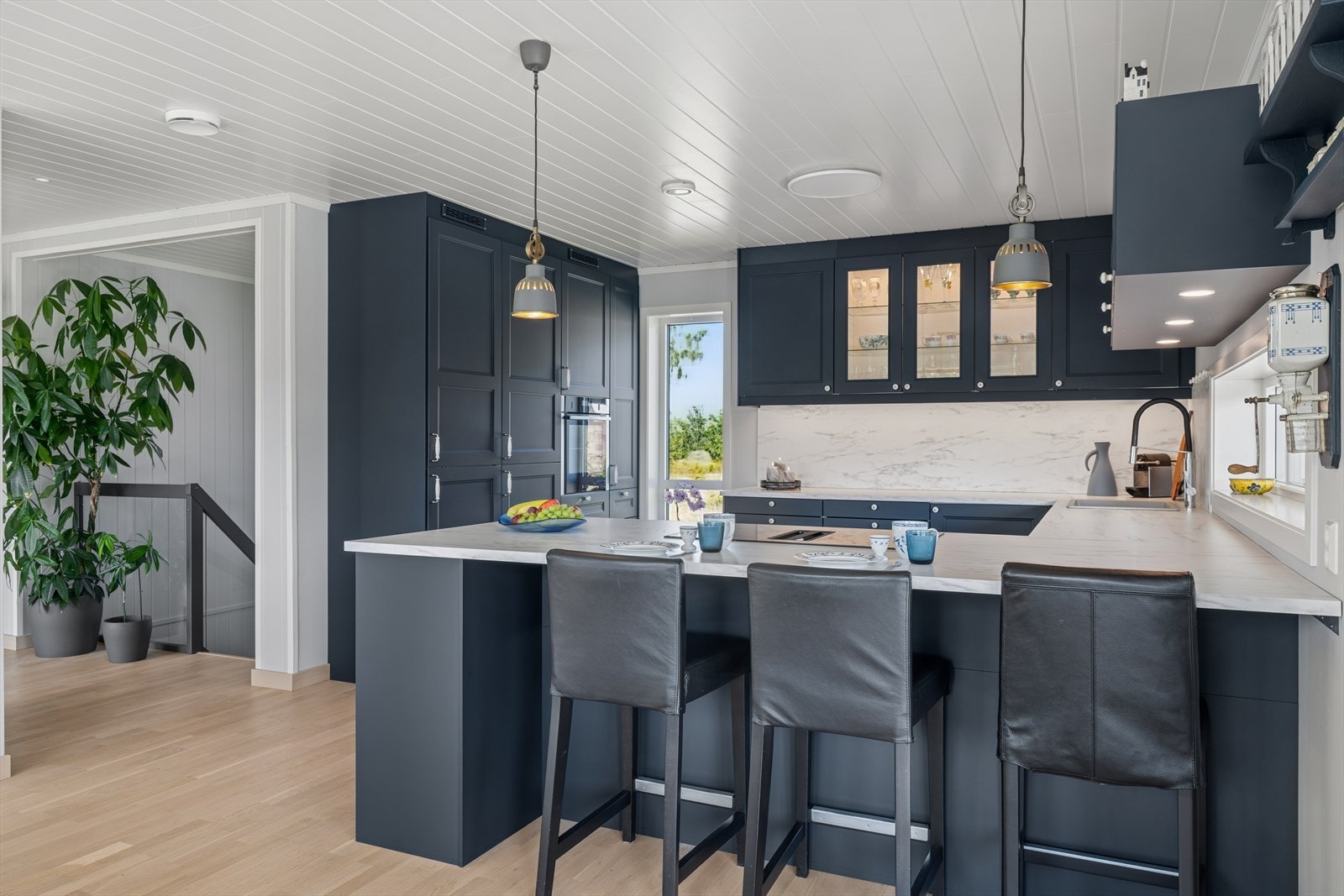 Kjøkkenet har mørke profilerte fronter med lys benkeplate og backsplash i lik utførelse for et rent uttrykk Galleribilde