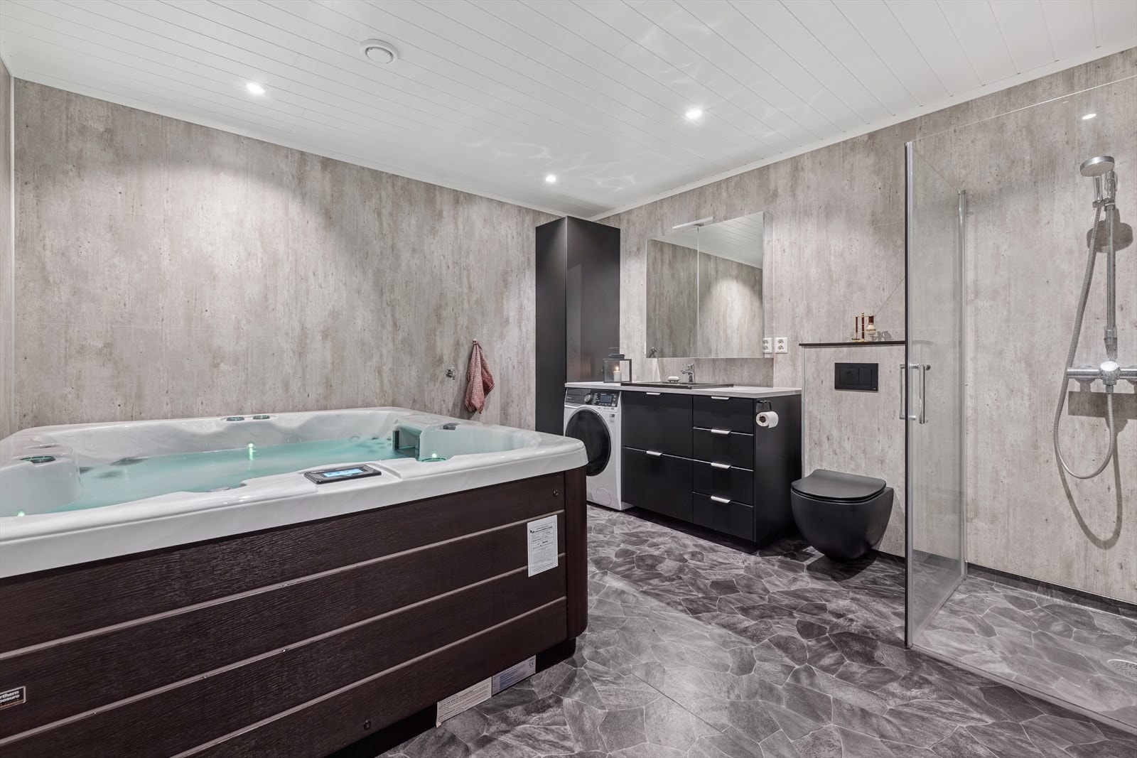 Rommet har en mørk innredning med nedfelt servant og god skapplass og plass/opplegg for vaskemaskin. Øvrig er det veggmontert toalett, dusjvegger/hjørne og Jacuzzi Galleribilde