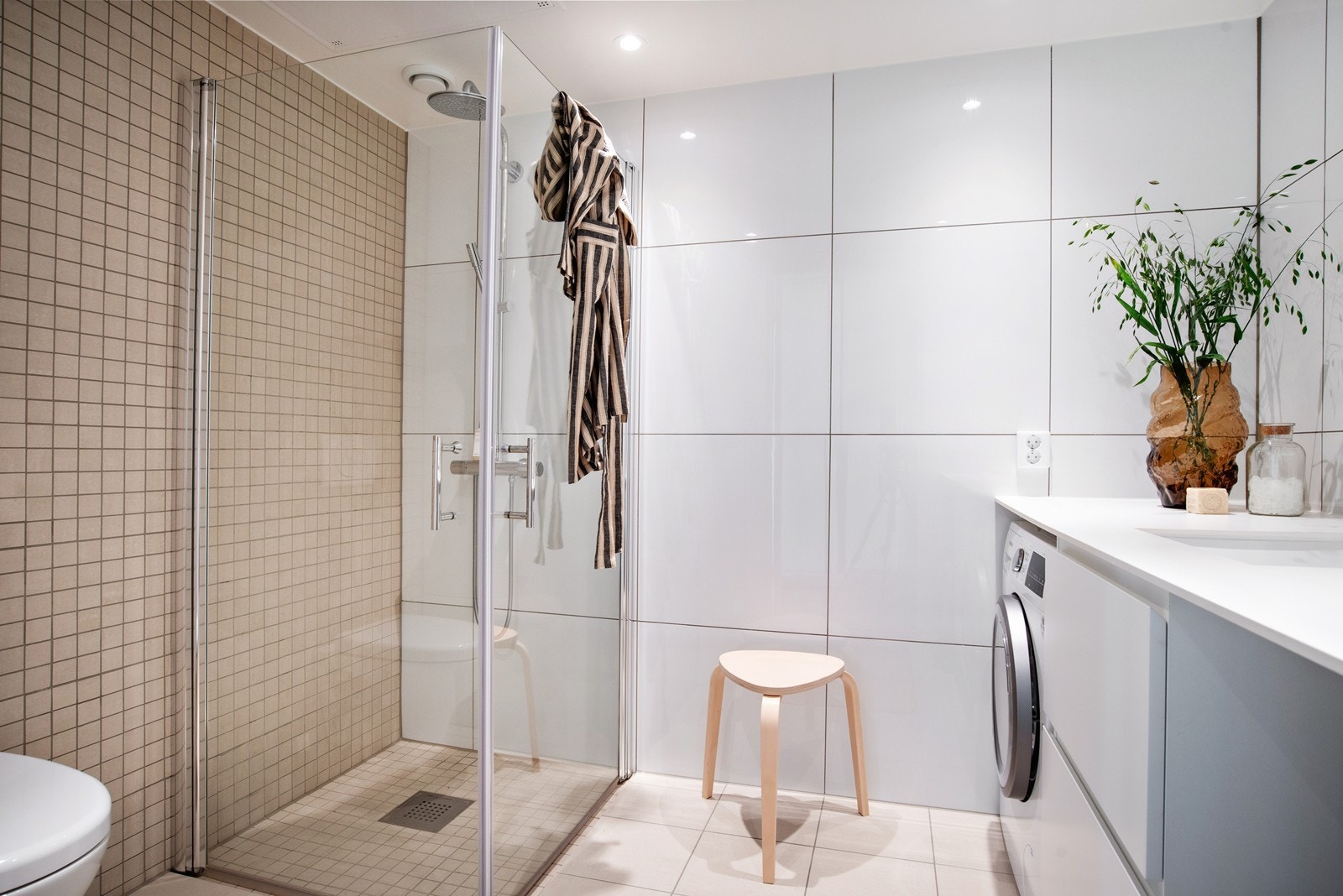 Stort bad med bred servantbenk og opplegg for vaskemaskin. WC og dushjørne. Galleribilde