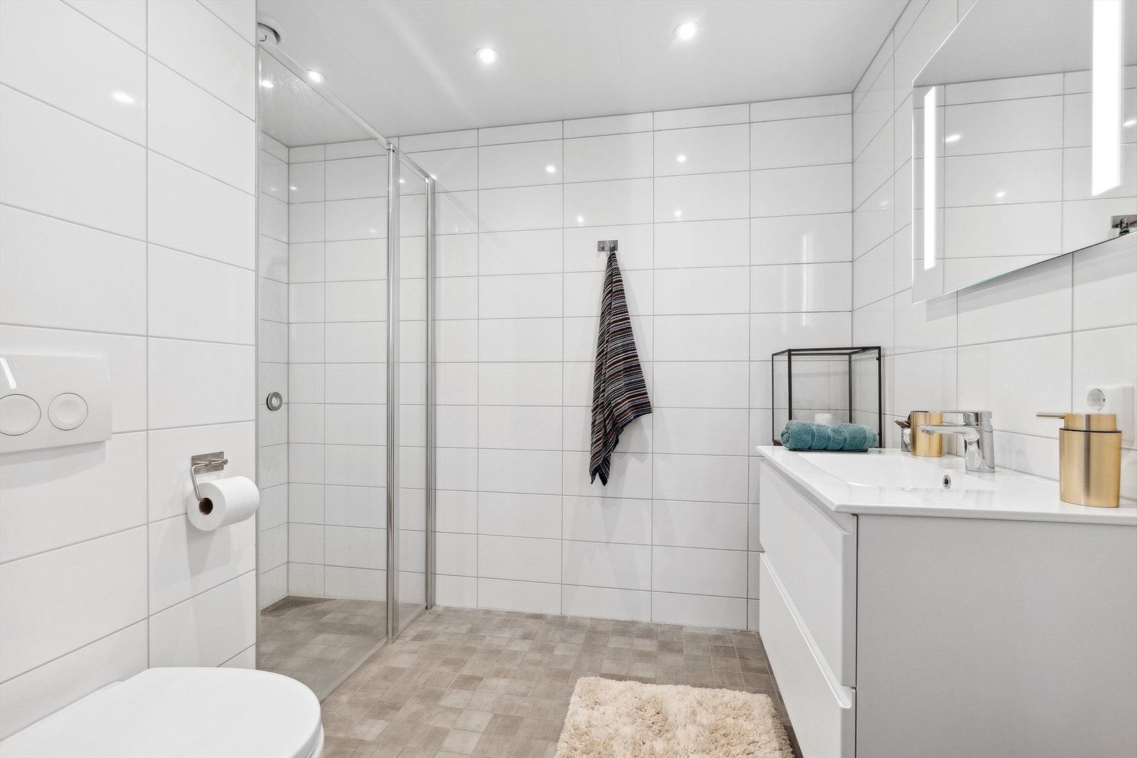 Baderomsinnredningen har god oppbevaringsplass, hvit servantløsning med speil og ekstra belysning. Dusjhjørne med glassdører. Gjennomgående stilrette fargevalg. Galleribilde