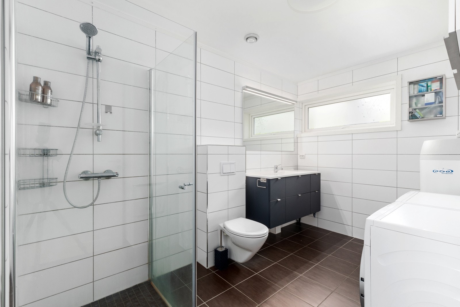 Badet er flislagt med dushjørne, veggehengt toalett og servantskap. Galleribilde