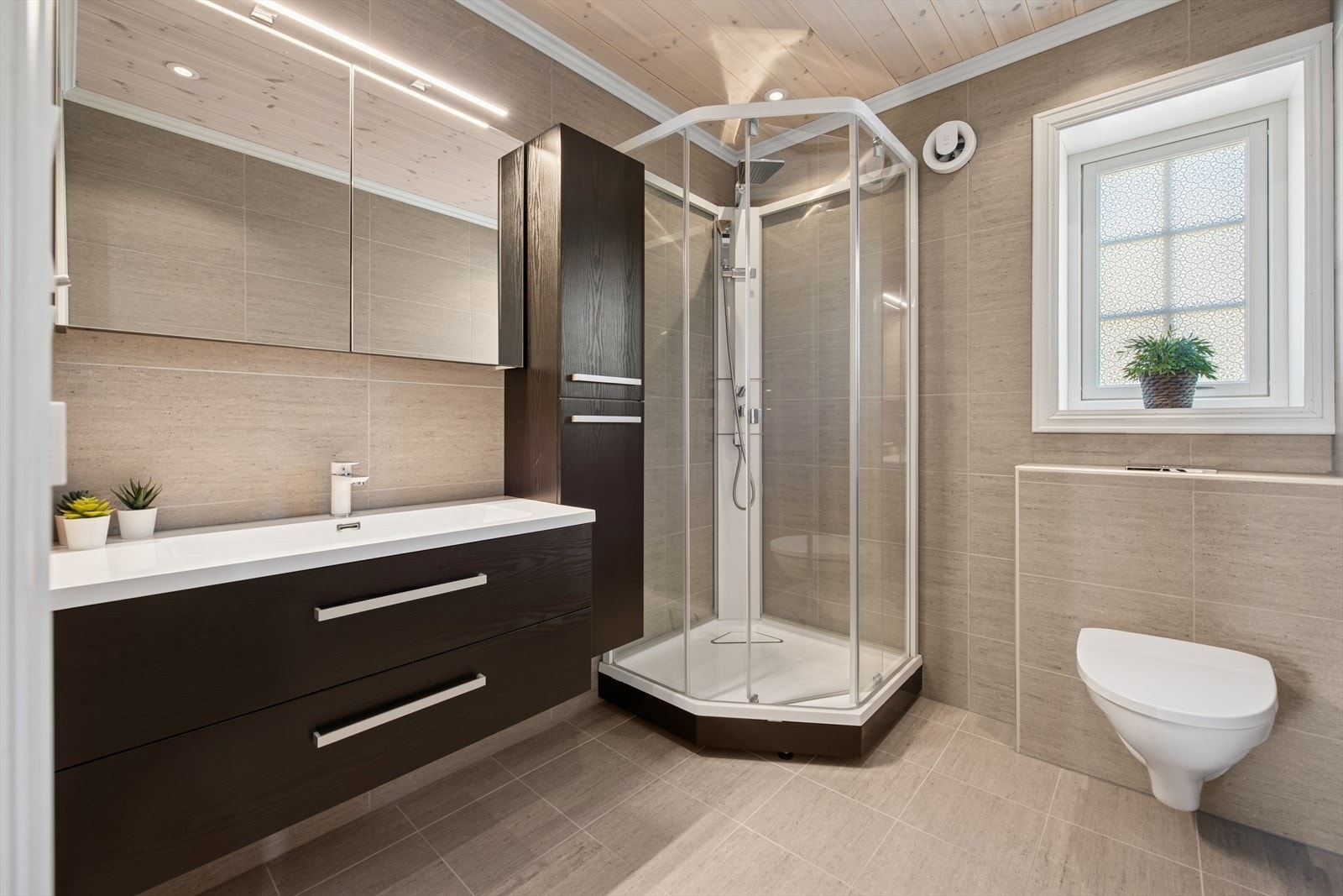 Baderommet er utstyrt med dusjkabinett, vegghengt toalett og servant med tilhørende innredning. Det finnes også overskap med speil og lys, gulvvarme for ekstra komfort. Galleribilde