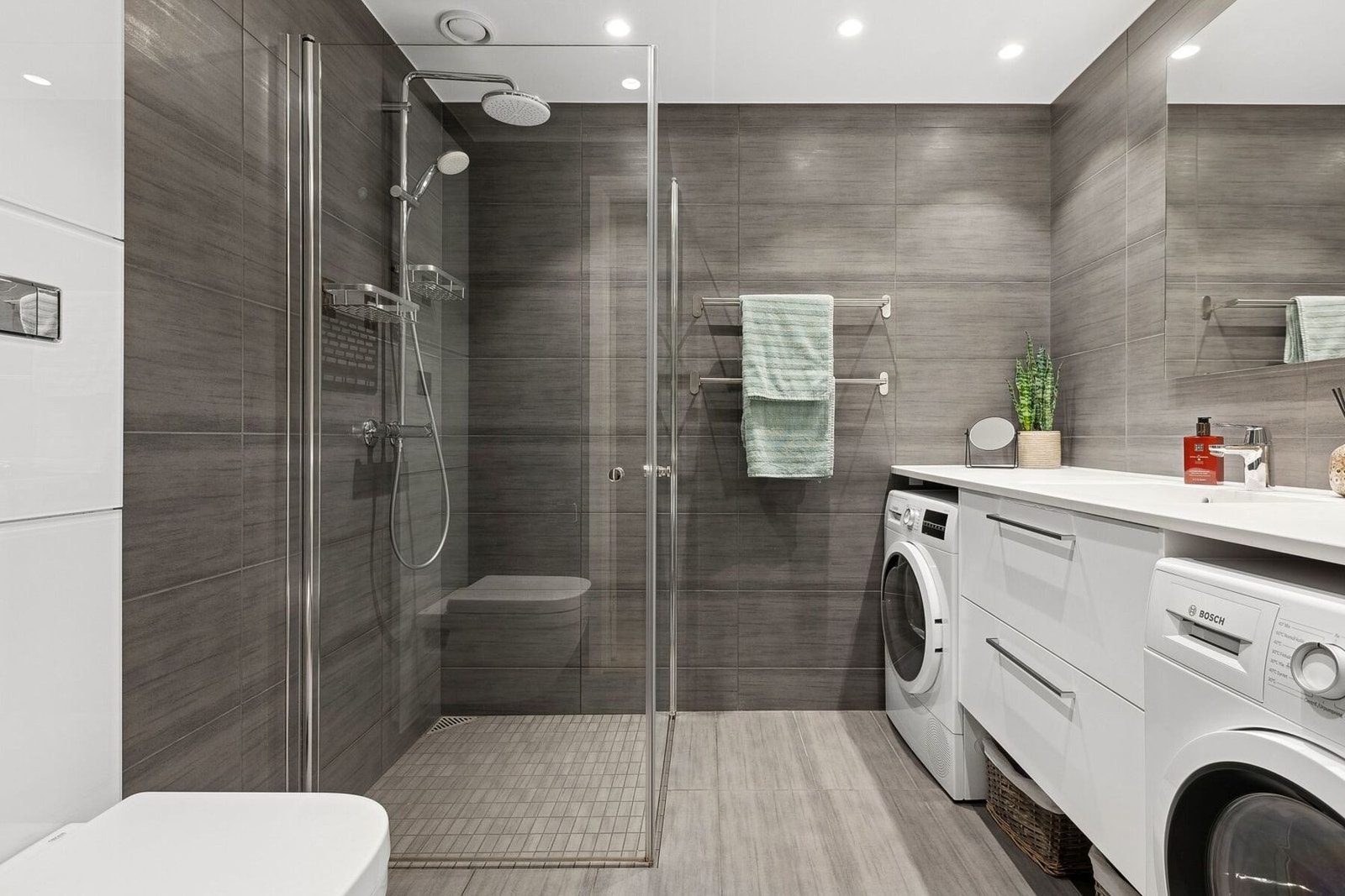 Badet har lekre fliser på gulv og vegger, servant med underskap, dusjvegger, opplegg for vaskemaskin, vegghengt toalett m.m. Galleribilde