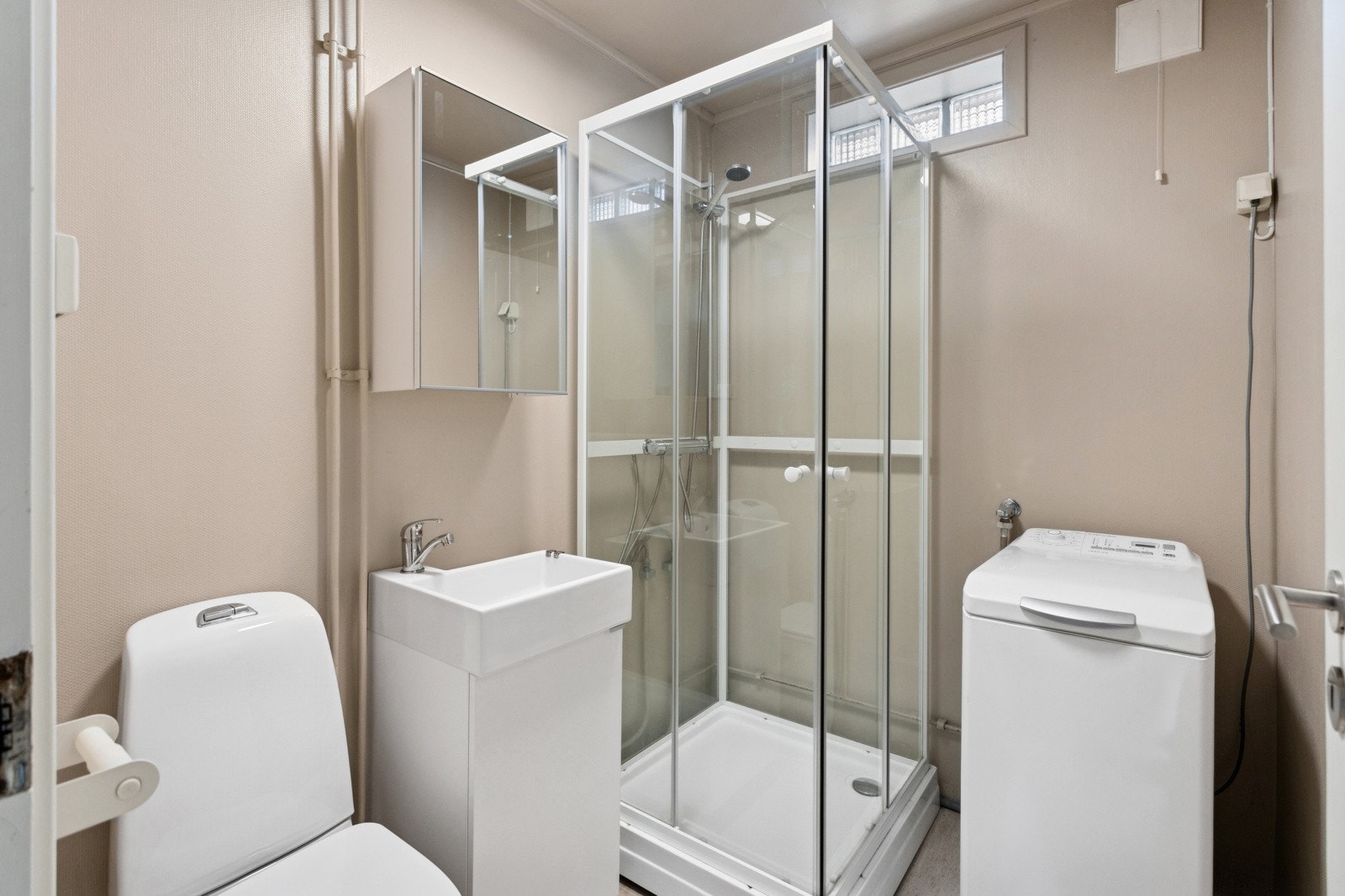 Bad i hybelen med belegg på gulv og vegger med malte plater og malt strie. Her finner du toalett, dusjkabinett og baderomsinnredning med heldekkende servant og speilskap på vegg. Opplegg for vaskemaskin. Galleribilde