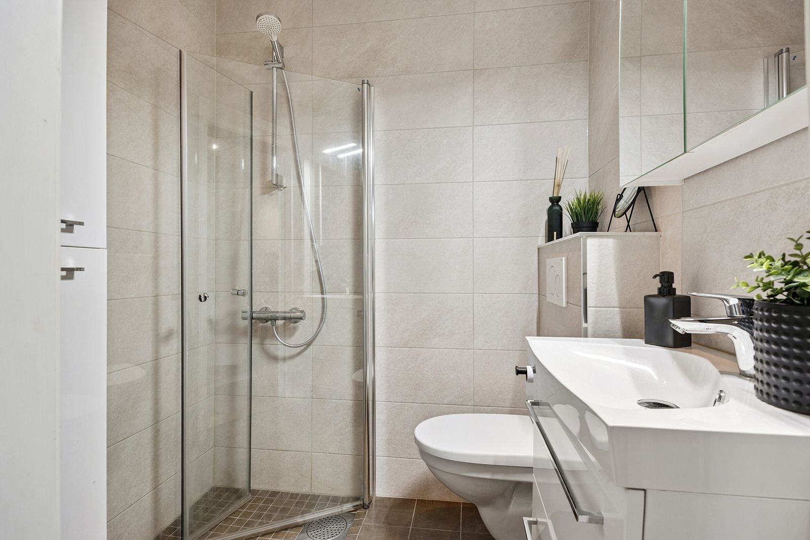 Pent bad med innfellbare dusjdører, vegghengt WC og servant med underskap. Galleribilde