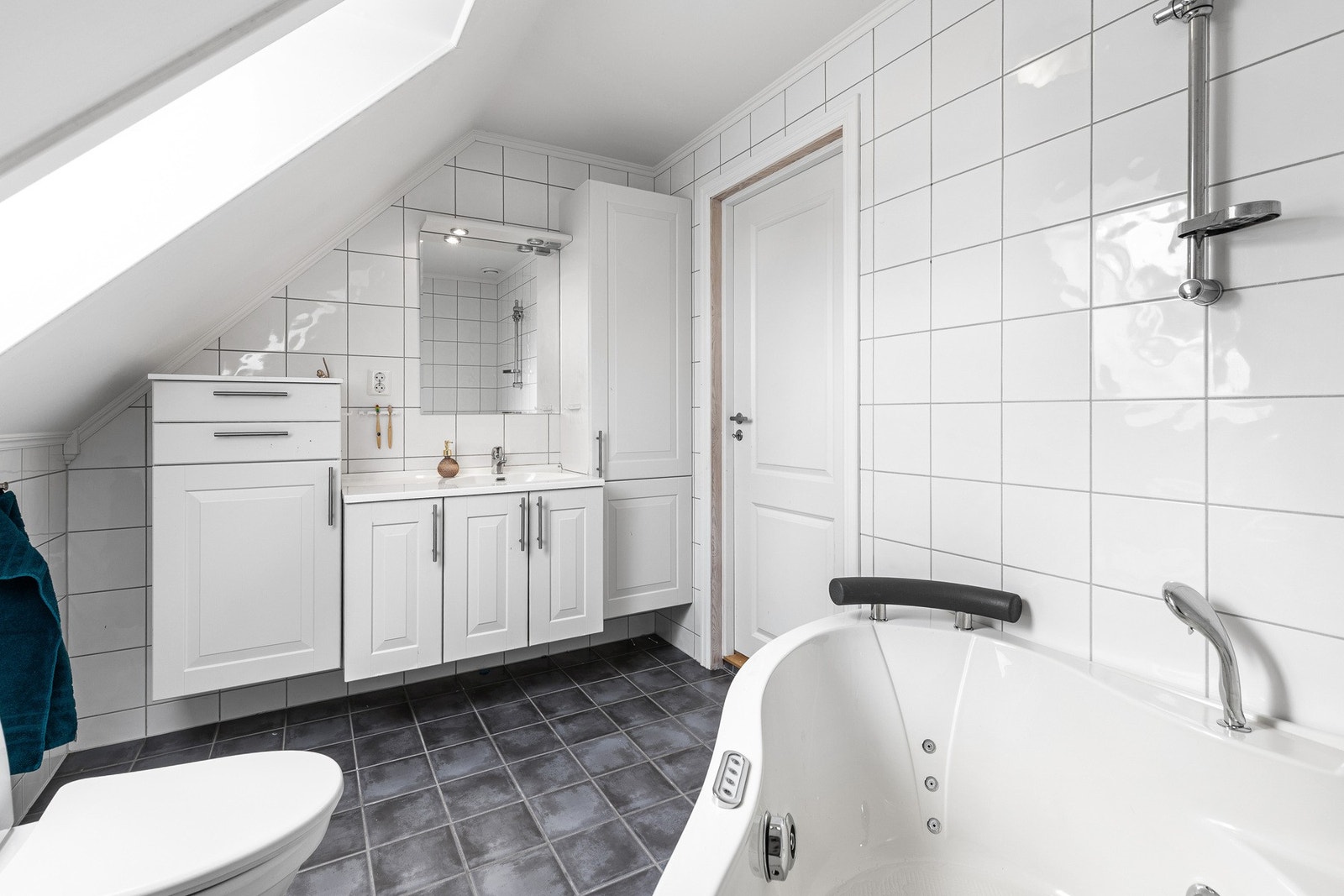 I 2. etasje finner du et romslig familiebad med hvite fliser, mørke gulvfliser og takvindu som slipper inn naturlig lys. Galleribilde