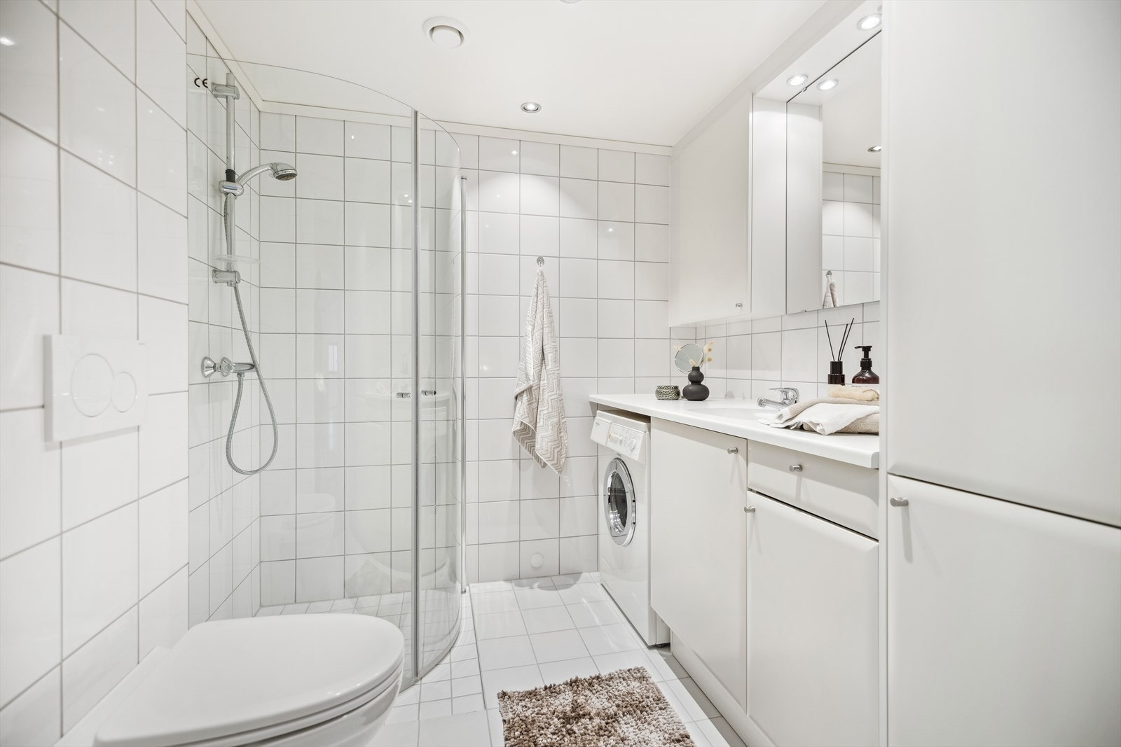 Badet fra hallen er flislagt med vannbåren gulvvarme, dusjhjørne med svingbare glassdører, vegghengt toalett og servantinnredning. Galleribilde