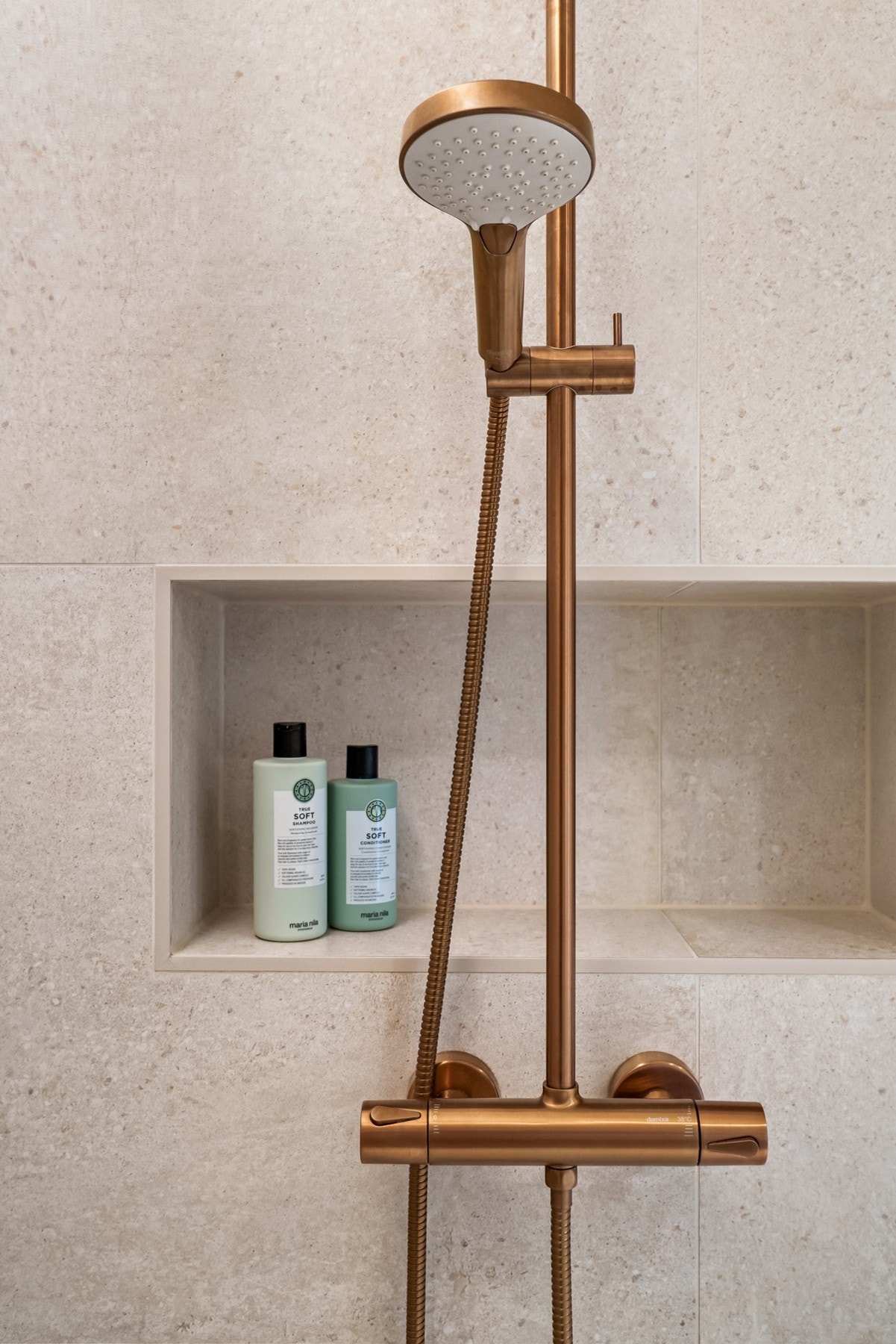 Badet har lyse materialvalg, naturtro innredning og detaljer i lekker bronsefinish. Dusjen er utstyrt med fastfelt glassvegg, innfelt veggnisje og garnityr med regnfall, samt hånddusj. Galleribilde