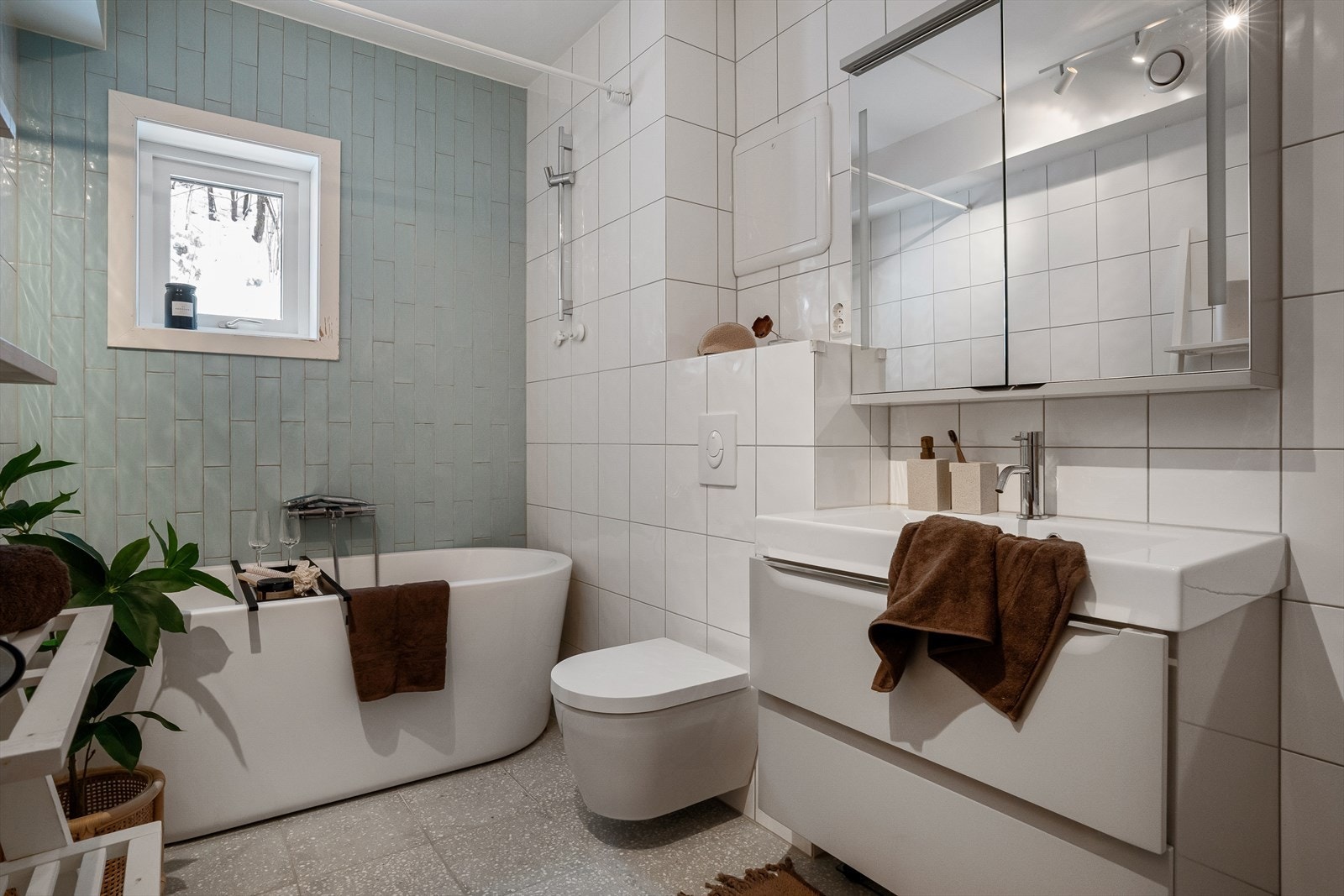 Rommet er innredet med servant i møbel, speilskap med lys, vegghengt toalett og badekar Galleribilde