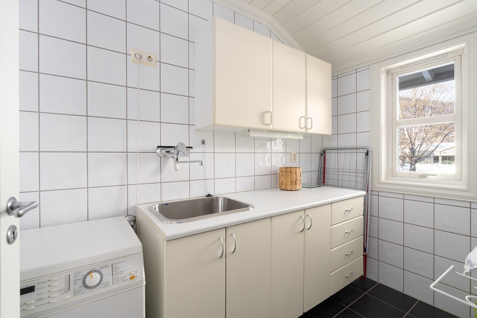 Vaskerom med flislagte overflater og varme i gulv. Skapplass, skyllekum og opplegg for vaskemaskin. Galleribilde