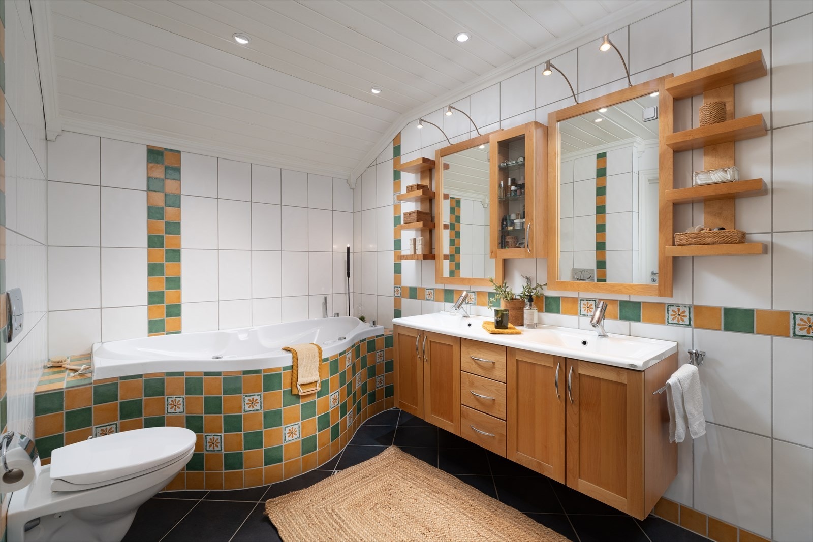 Badet har flislagte overflater og varme i gulv. Servantseksjon, vegghengt toalett, massasje badekar og dusjhjørne. Galleribilde