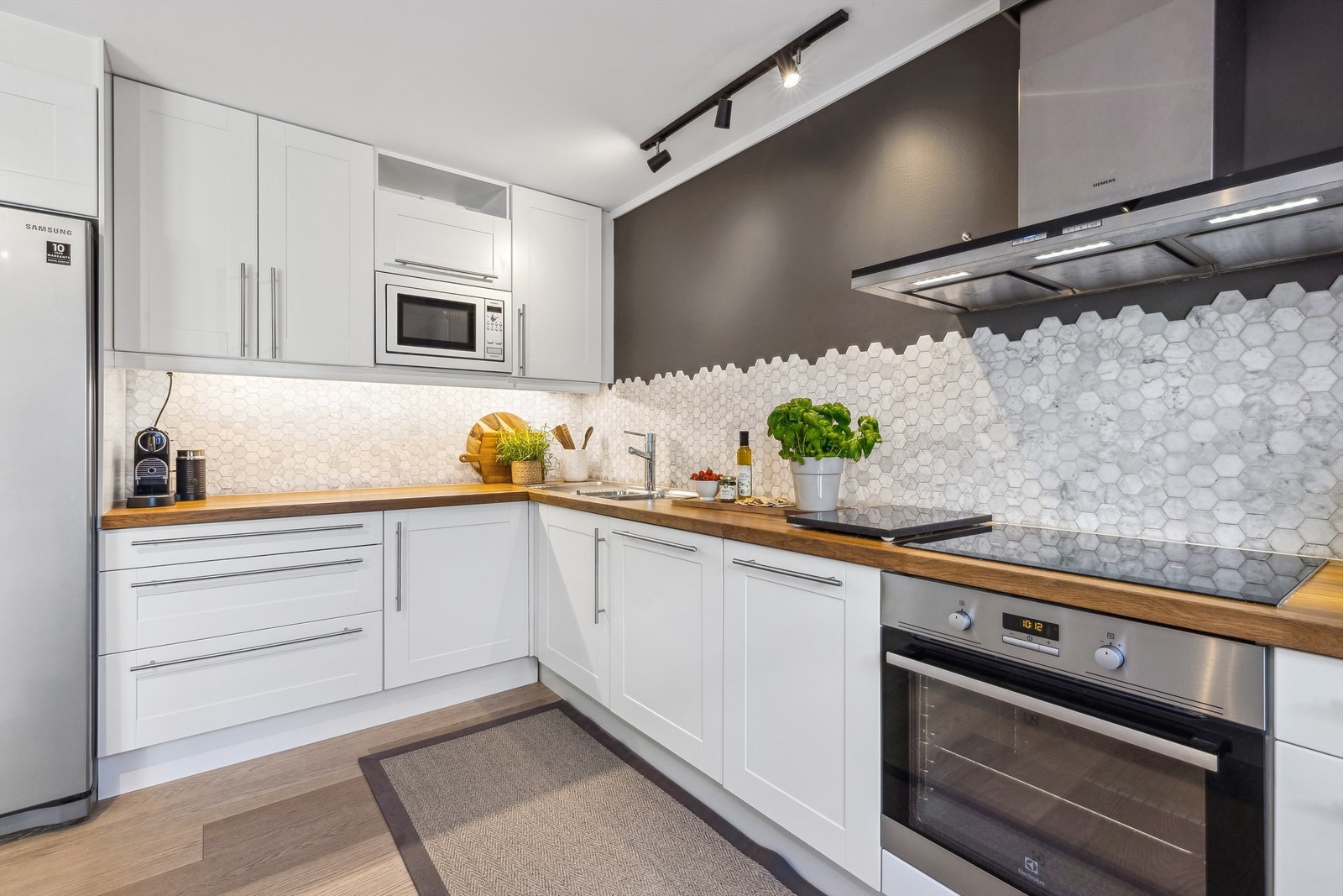 Praktisk belysning under overskap og integrerte hvitevarer som induksjonstopp, stekeovn, veggmontert kullfilterventilator i stål, oppvaskmaskin og mikrobølgeovn samt side-by-side kjøl-/fryseskap. Galleribilde