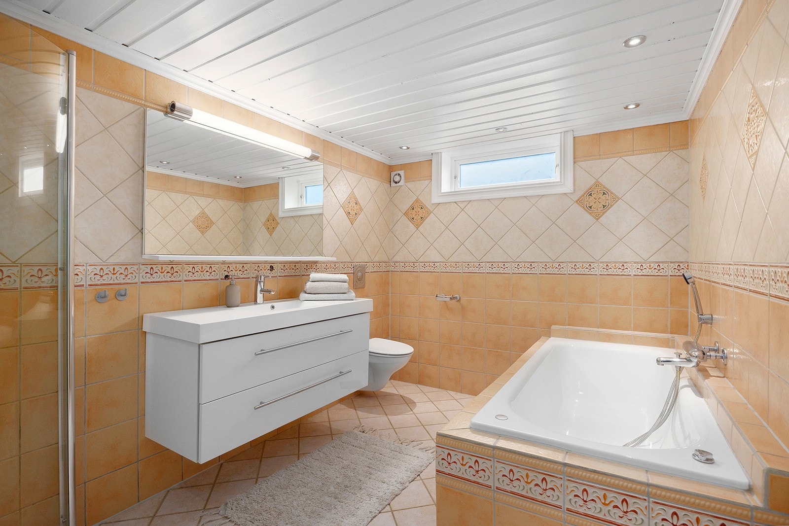 Stort baderom med innfliset badekar og separat dusjhjørne med buede dusjdører, samt veggmontert klosett. Galleribilde