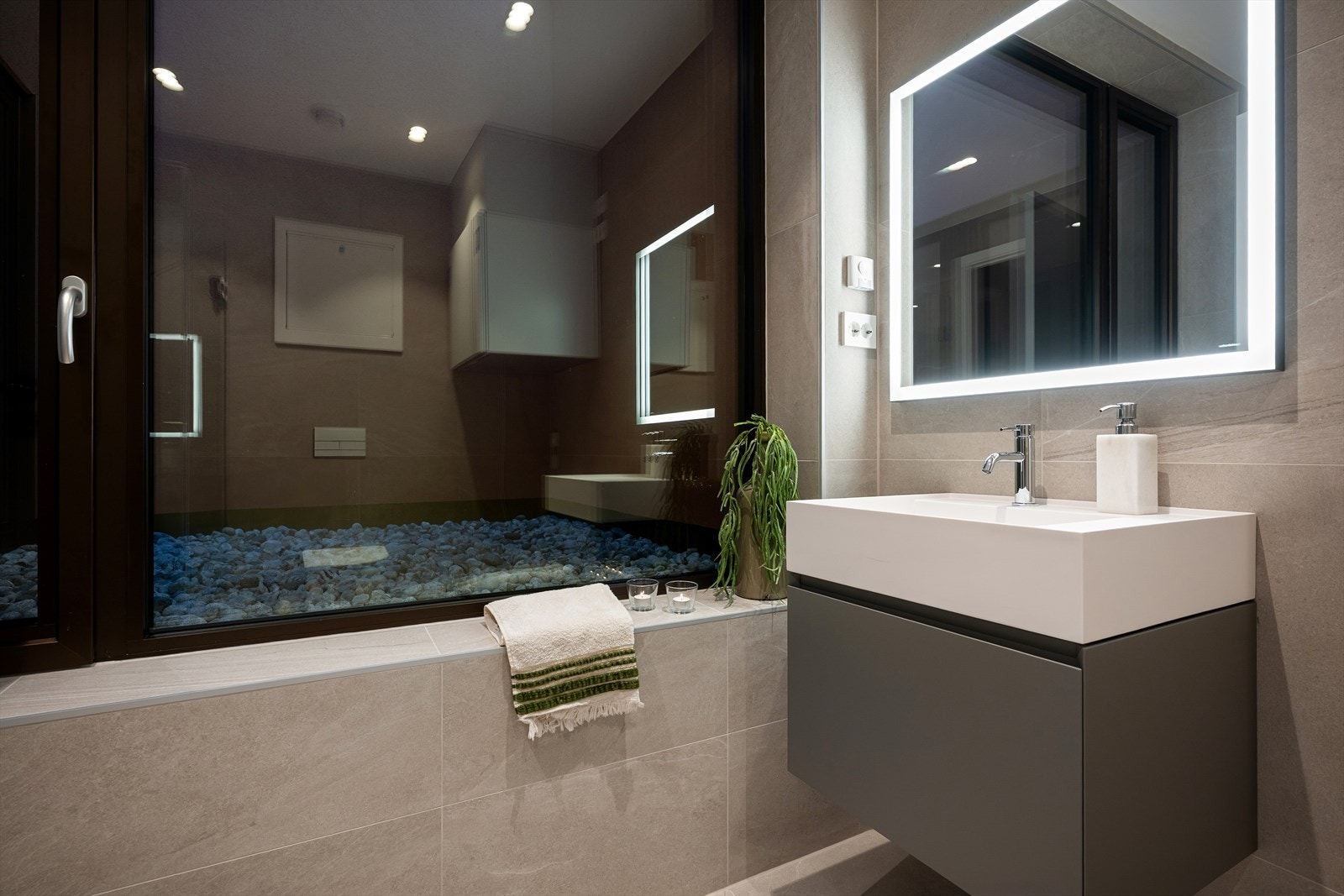 Badene er innredet med store fliser, downlights og speil med integrert belysning Galleribilde