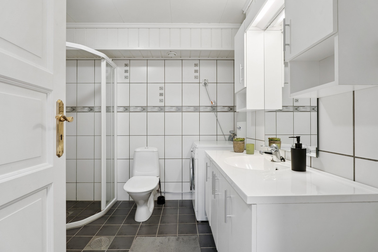 Badet er helfliset med elektriske varmekabler i gulvet. Rommet er innredet med servant nedfelt i baderomsinnredning, toalett og dusjvegger med tett bunnlist. Opplegg for vaskemaskin. Galleribilde