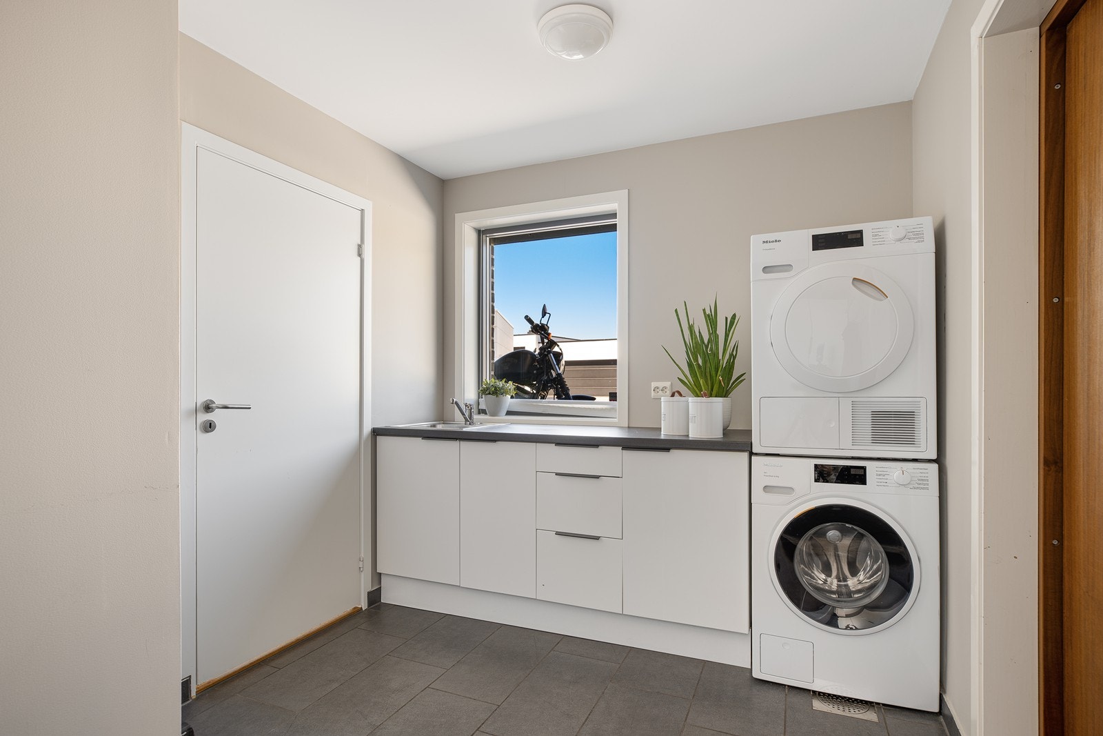 Praktisk og romslig vaskerom med egen inngang. Fliser på gulv og lyse gipsvegger. Opplegg for vaskemaskin Galleribilde