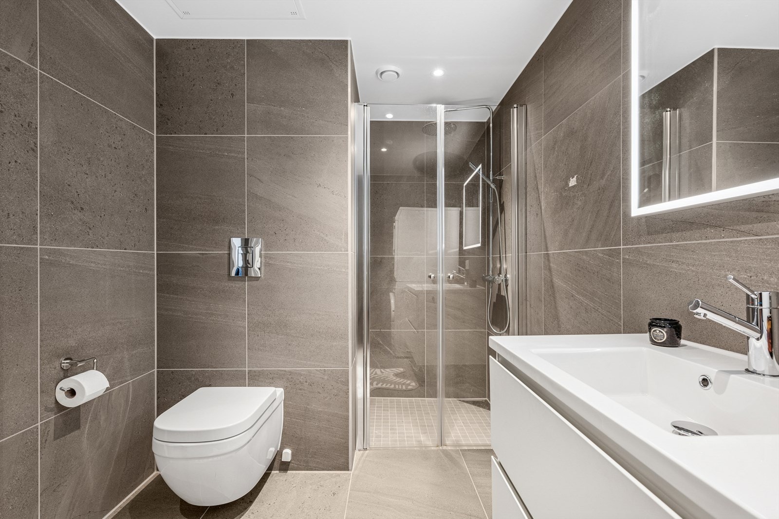 Innredningen består av speil med lys, servant med skuffeseksjon, vegghengt skap, dusjnisje, vegghengt toalett og opplegg for vaskemaskin. Galleribilde