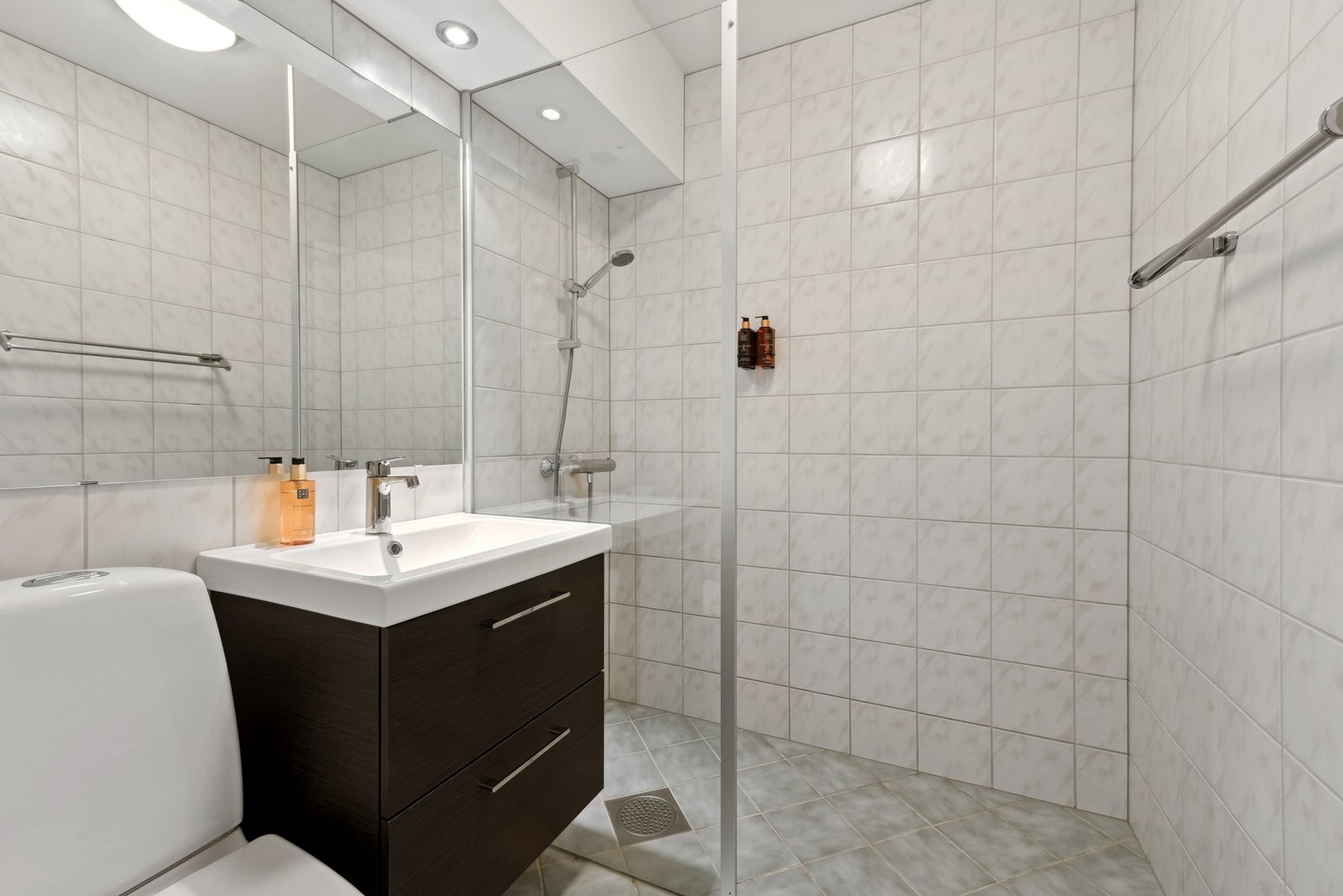 Baderommet er utstyrt med gulvstående toalett, vegghengt servantinnredning og dushjørne med dører. Galleribilde