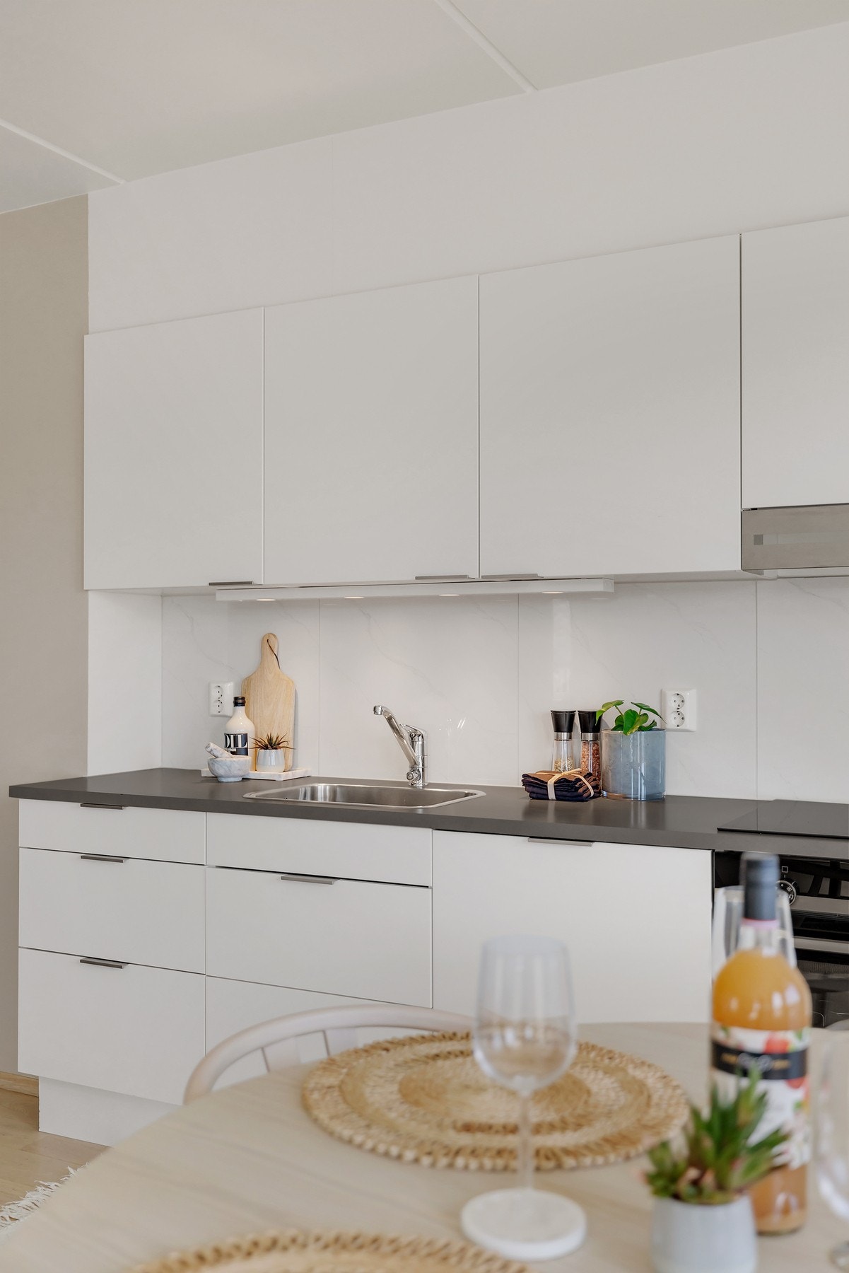 Kjøkkeninnredning fra Norema med slette lakkerte fronter, laminat benkeplate med fliser på bakvegg og rustfri oppvaskkum. Galleribilde