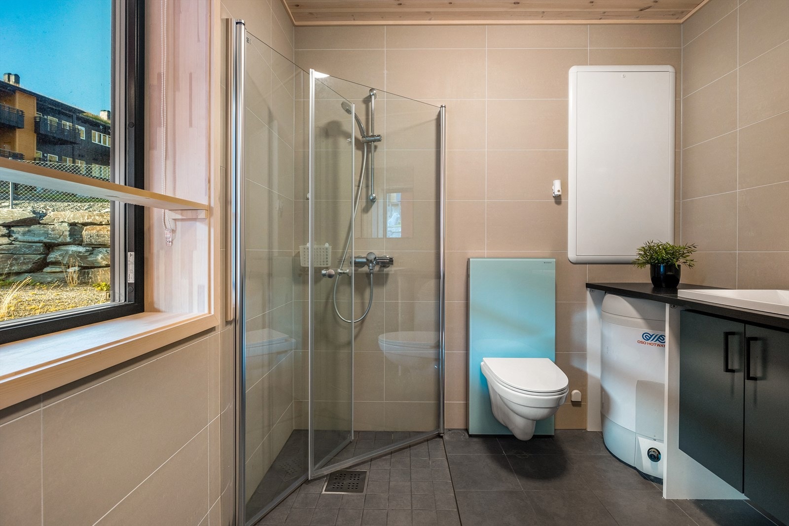 Badet holder en moderne og minimalistisk stil, med antrasittgrå gulvfliser og beige veggfliser som gir et rolig uttrykk. Galleribilde