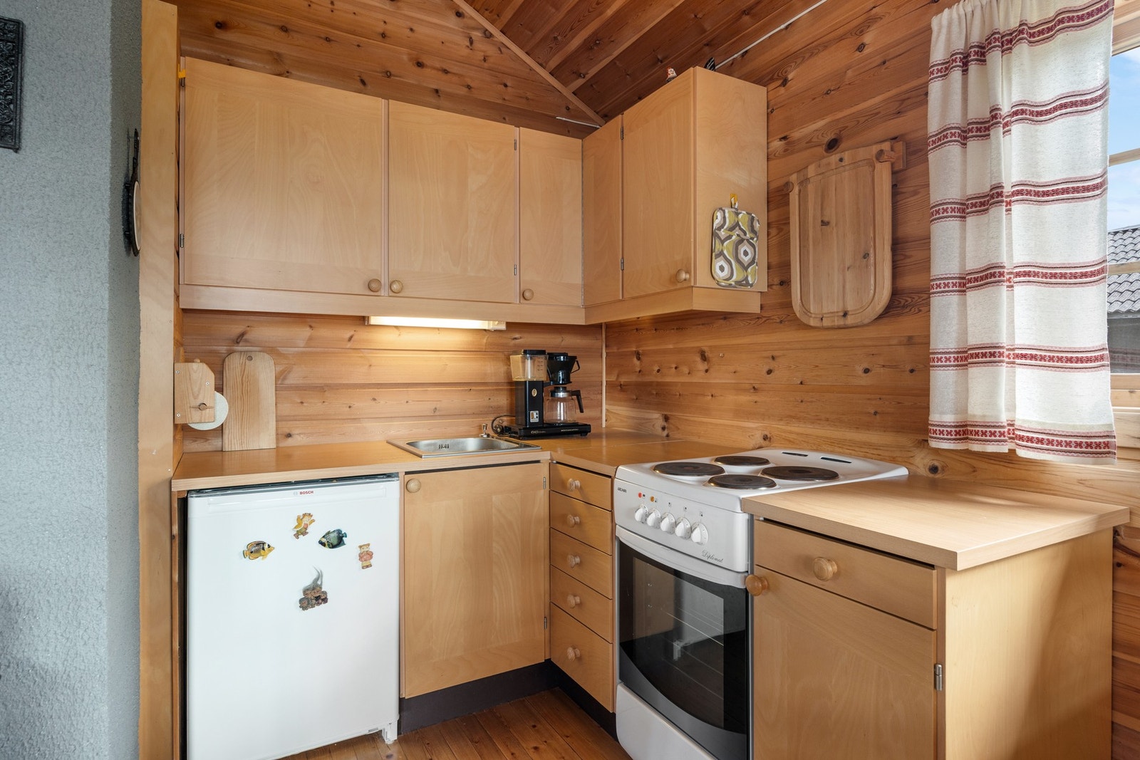 Enkel kjøkkeninnredning med avsatt plass for komfyr og kjøleskap. Sommervann fra vannpost. Galleribilde