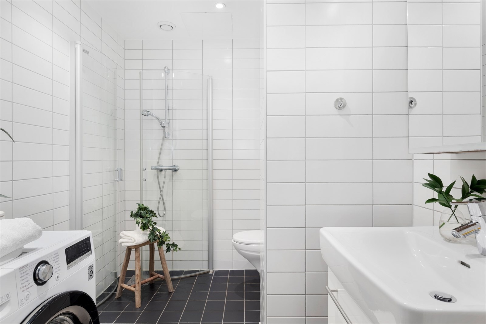 Stilrent fliselagt bad med elektriske varmekabler i gulvet og funksjonelle løsninger som dusjhjørne, servant med underskap og opplegg for vaskemaskin. Galleribilde