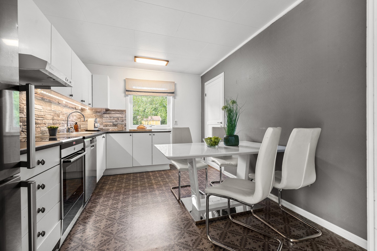 Innredningen er hvit og tidløs med slette fronter og sorte detaljer, samt steinfliser mellom benkeplate og overskap Galleribilde