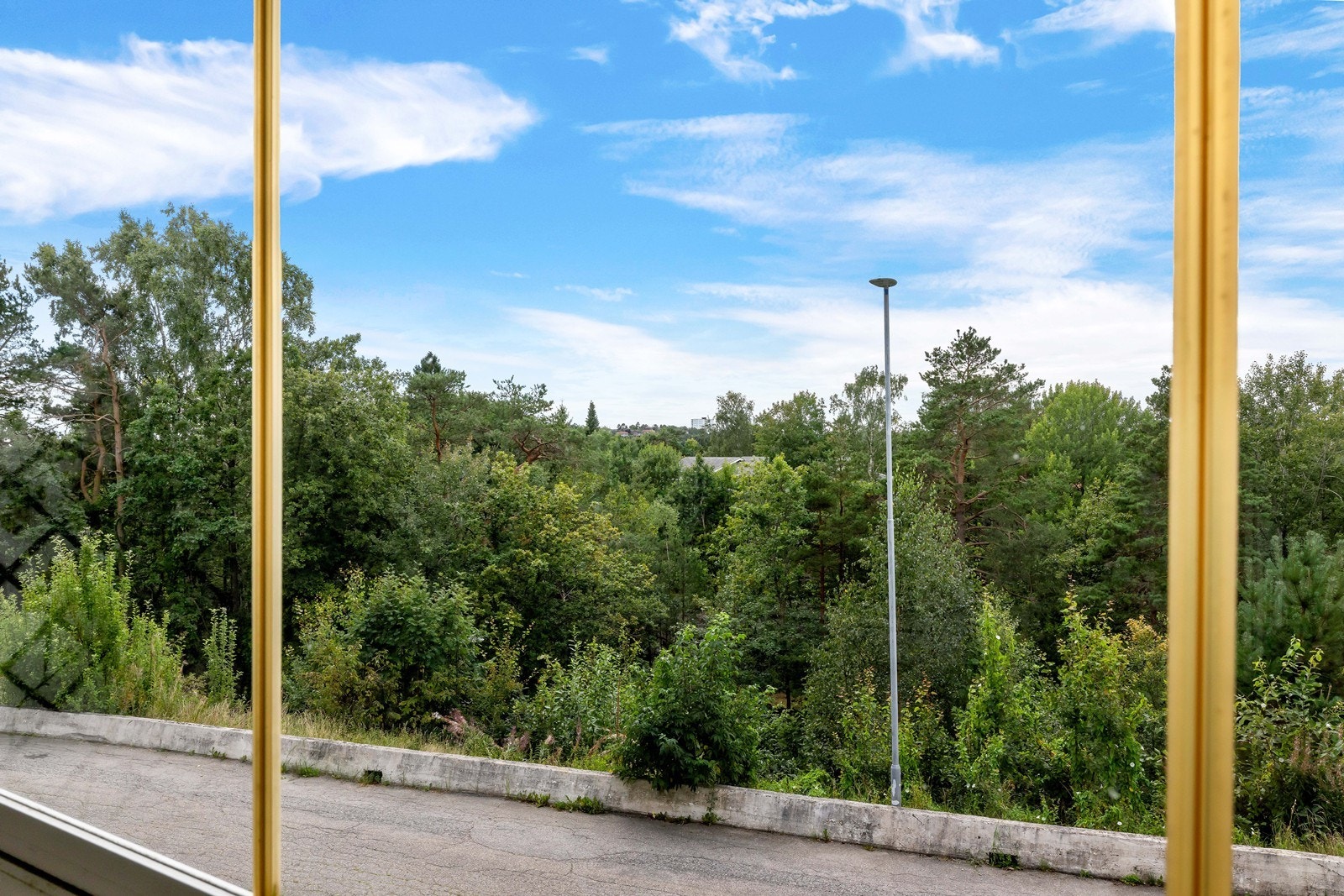 Utsikt fra balkong. Området nedenfor blokken (under trekronene i dette bildet) er pent opparbeidet med lekeplass/tuftepark, plener, idrettsplass og fine turstier. Galleribilde
