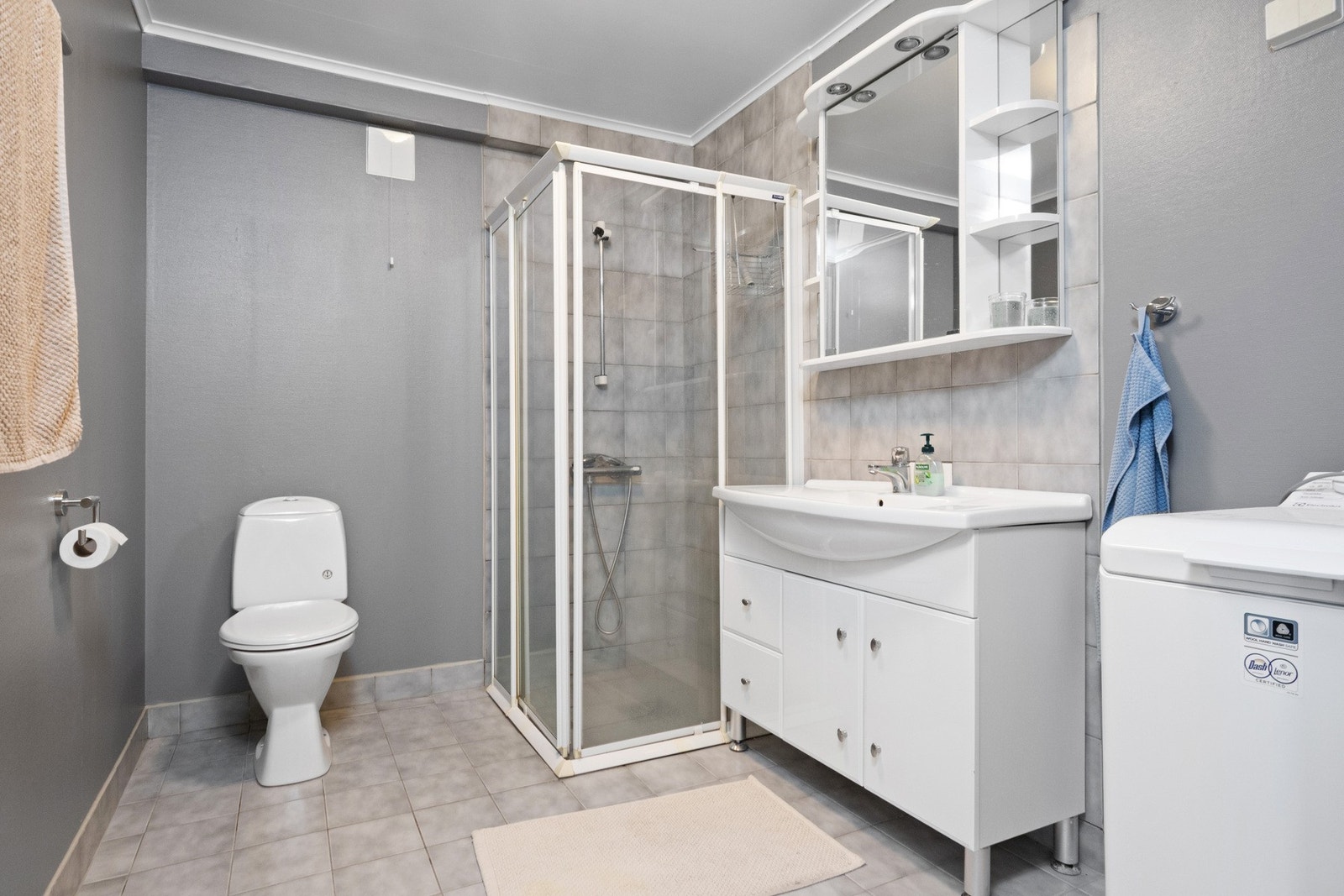 Badet i utleiedelen har gråmalt tapet på veggene og grå fliser på gulv med sluk og gulvvarme. Galleribilde