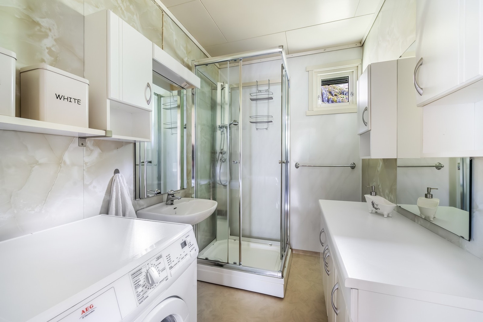 Lyst og funksjonelt bad med baderomsplater og praktisk dusjkabinett. Rommet er kombinert med vaskerom og har opplegg for vaskemaskin, noe som gir en arealeffektiv og brukervennlig løsning. Galleribilde