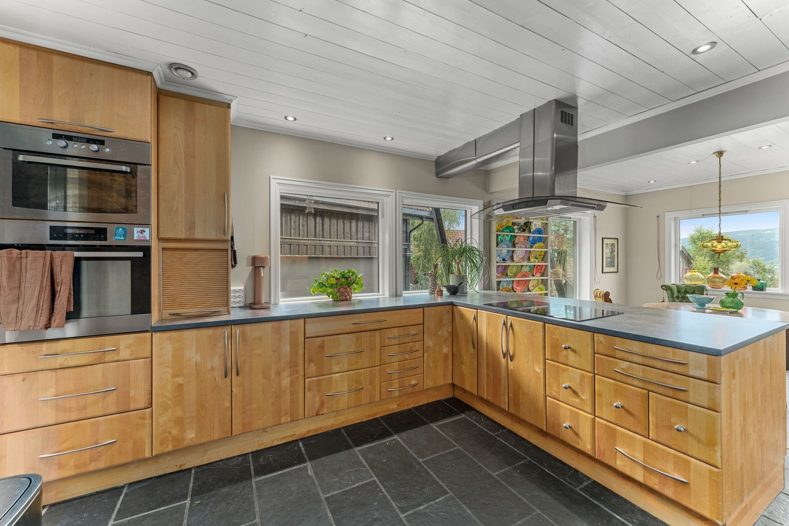 Kjøkkenet har store, slitesterke benkeplater som gir rikelig med arbeidsplass. Det er flere praktiske detaljer som integrert bokhylle, vinhyller og sjalusidører som raskt kan skjule kaffemaskin eller andre småapparater. Galleribilde