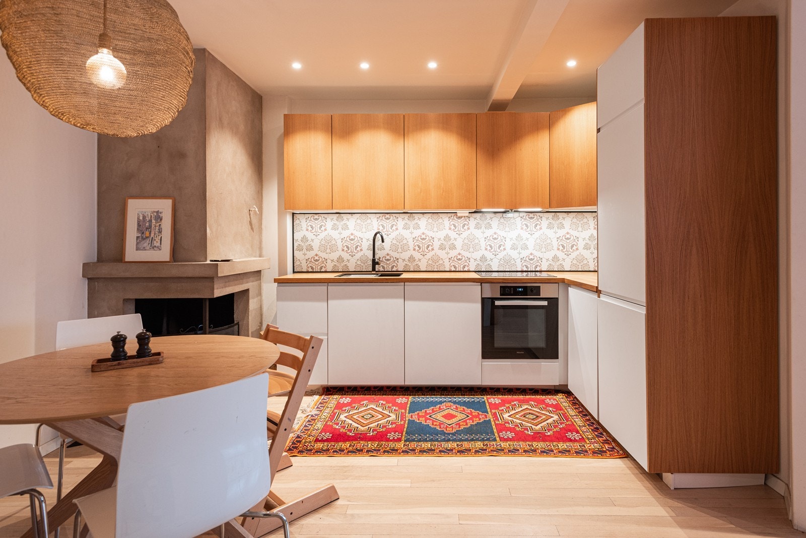 Et lyst og innbydende kjøkken med slette fronter og peis som gir en hyggelig stemning Galleribilde