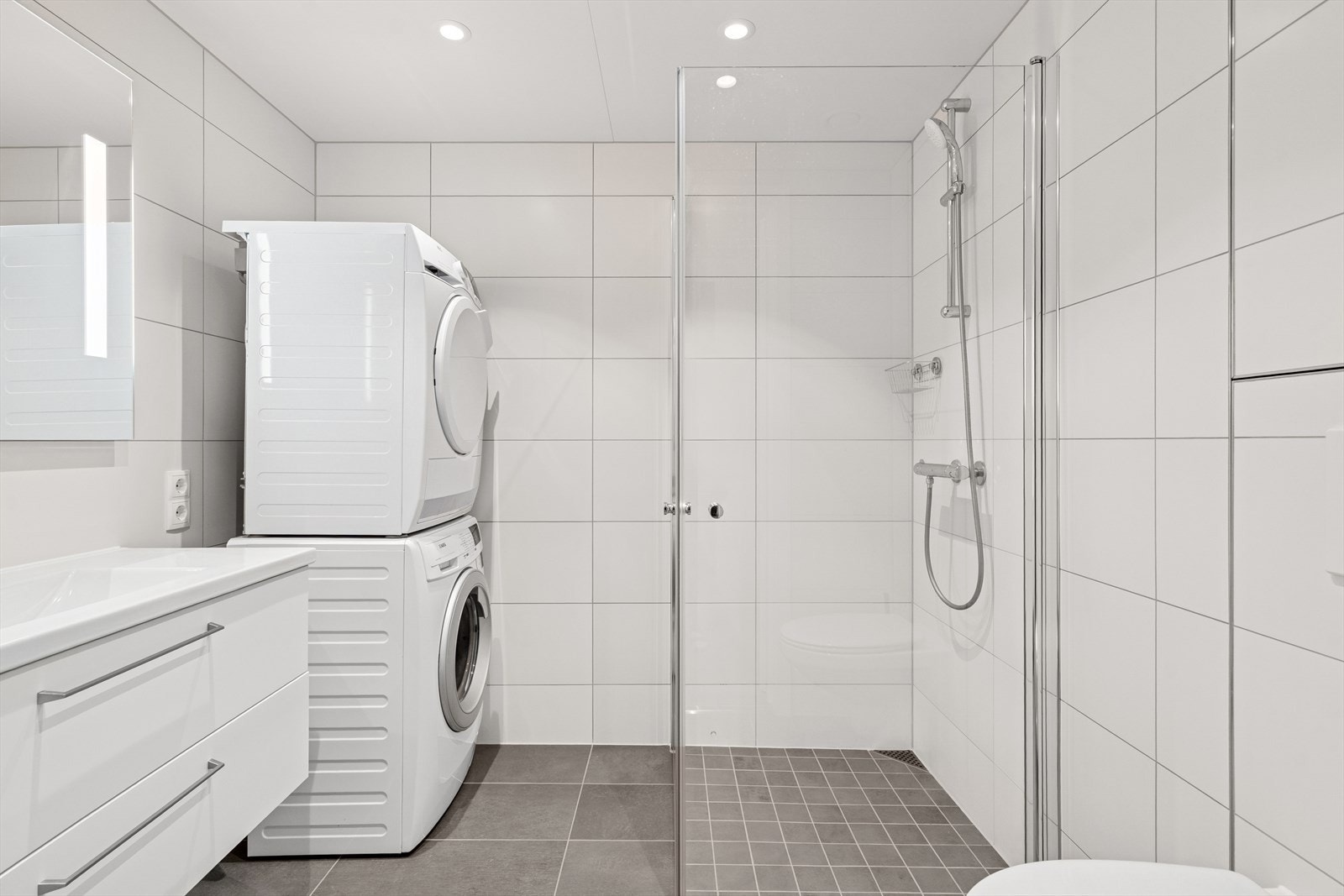 Badet er utstyrt med vegghengt toalett, dusjhjørne, opplegg til vaskemaskin og tørketrommel samt servant m/speil Galleribilde