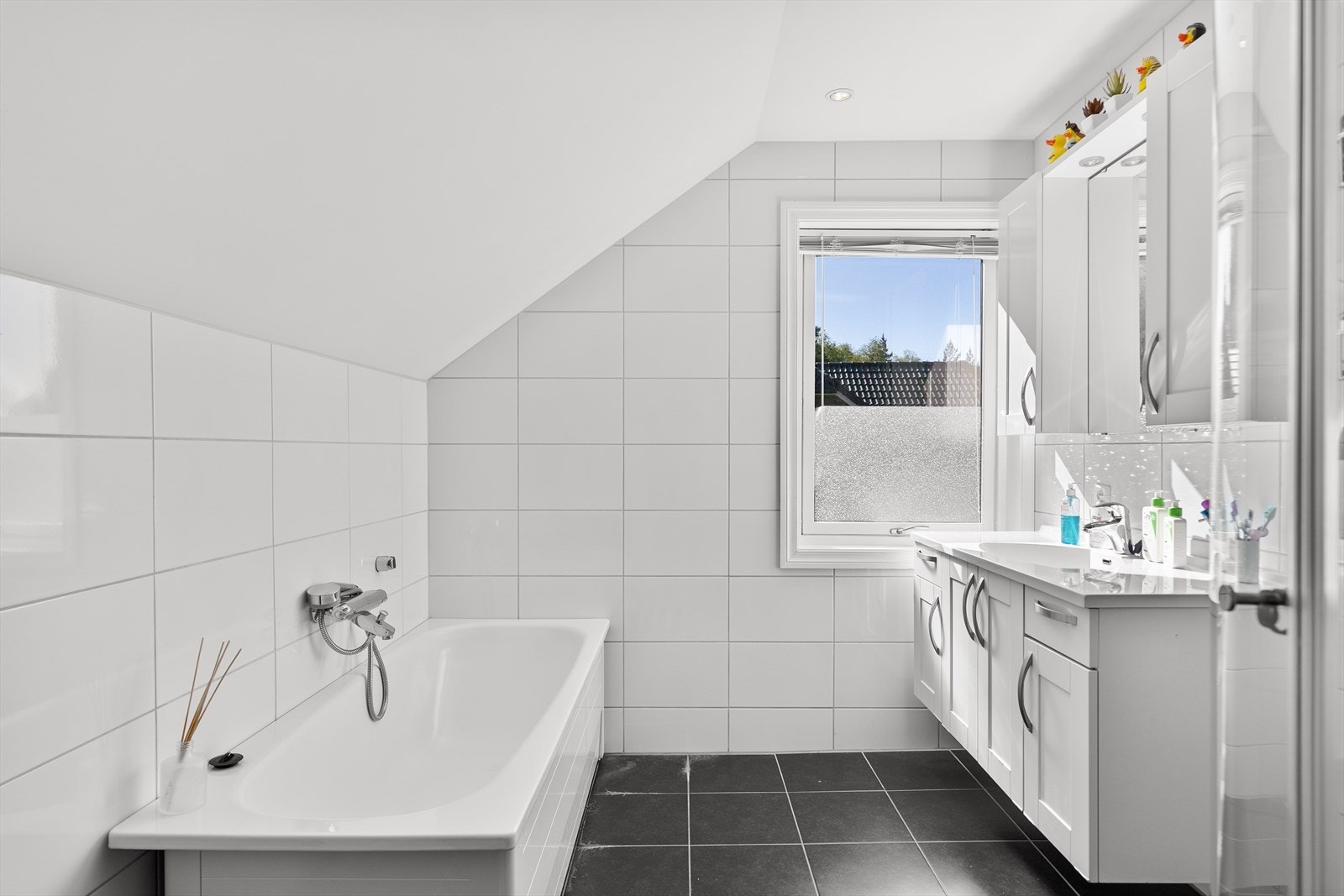 Badet inneholder dusj med foldedører, badekar, vegghengt toalett og helstøpt servant. Baderomsmøbler med profilerte fronter Galleribilde