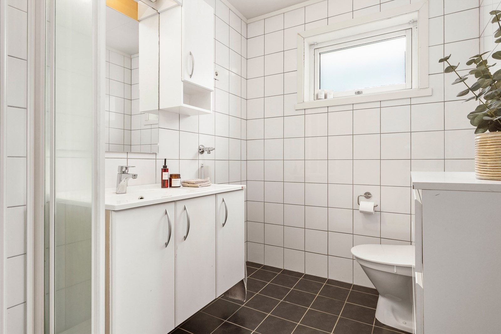 Badet inneholder dusjkabinett, toalett og baderomsinnredning. Flislagt med varmekabler i gulv. Galleribilde