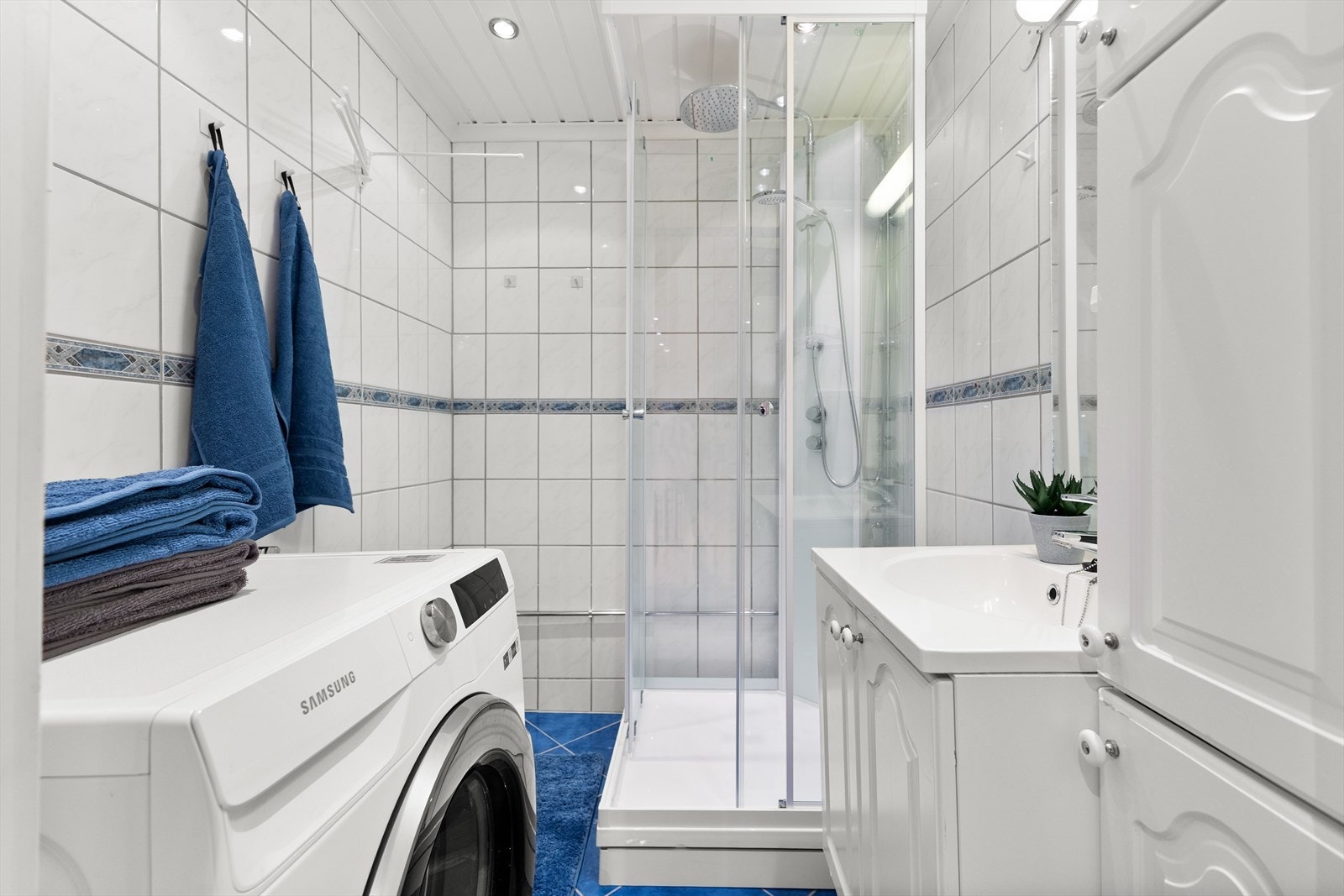 Bad med innredning bestående av nedfelt vask, benk- og høyskap og dusjkabinett. Galleribilde