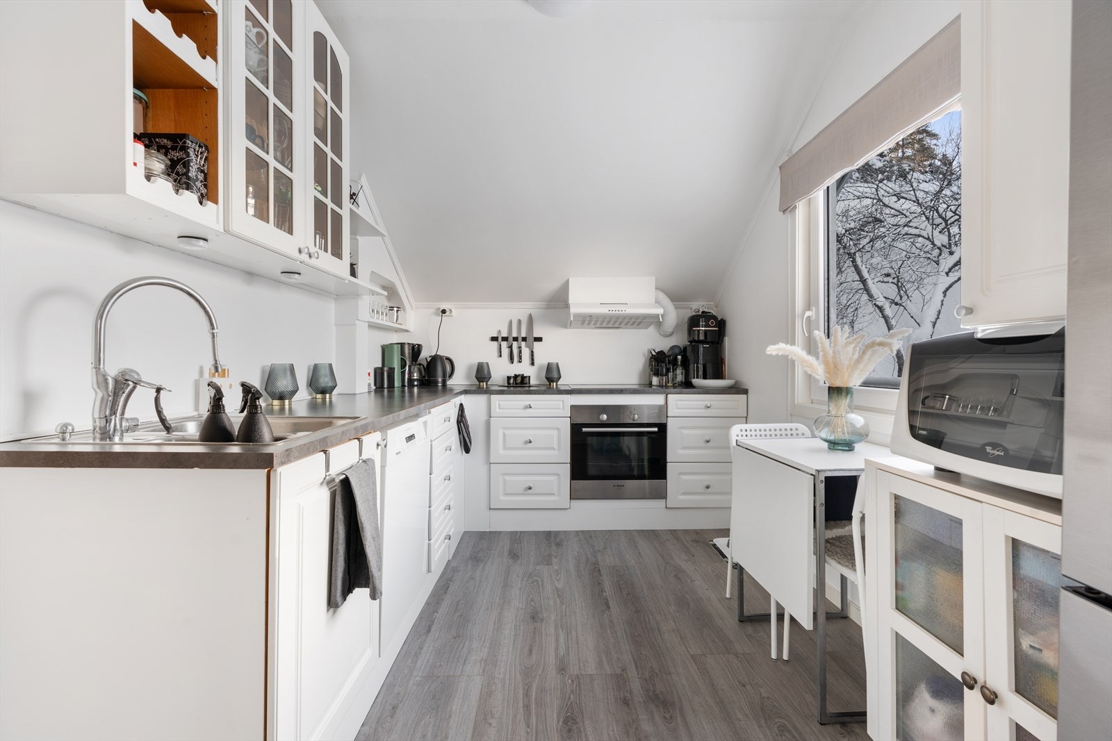 Kjøkkenet ligger i naturlig tilknytning til stuen og har en lys og tidløs innredning med hvite fronter og benkeplate i laminat Galleribilde