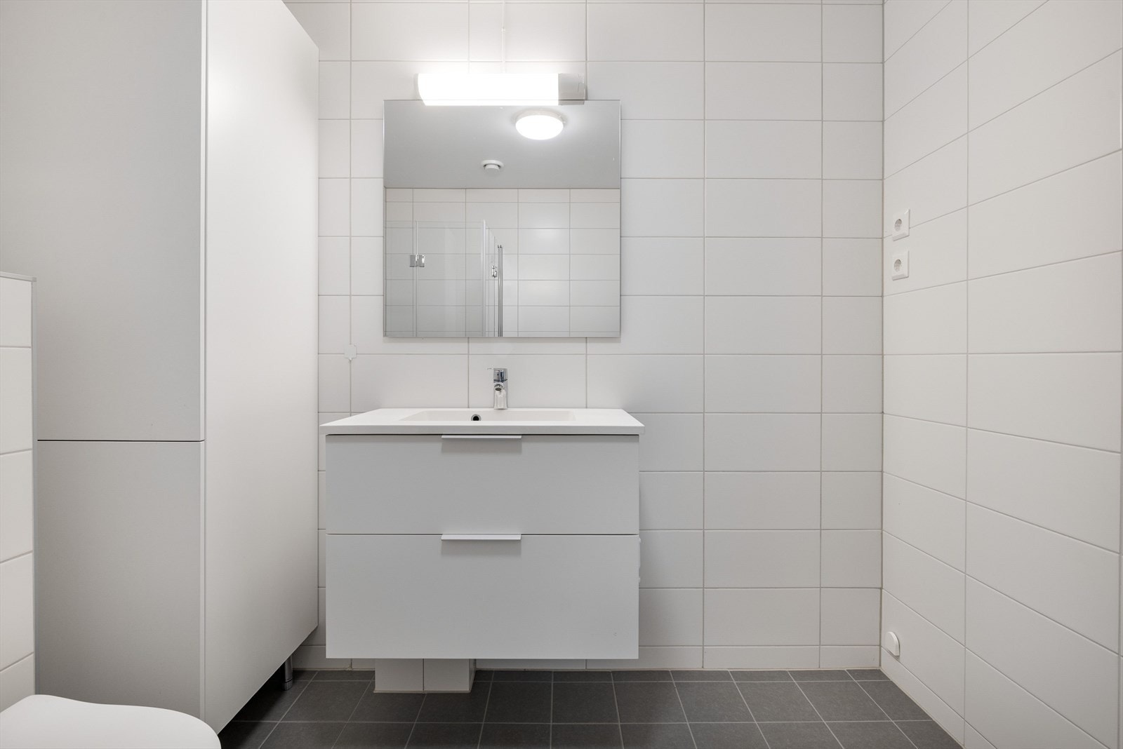 Moderne baderomsinnredning med skuffer og heldekkende servant, speil med belysning over. Galleribilde