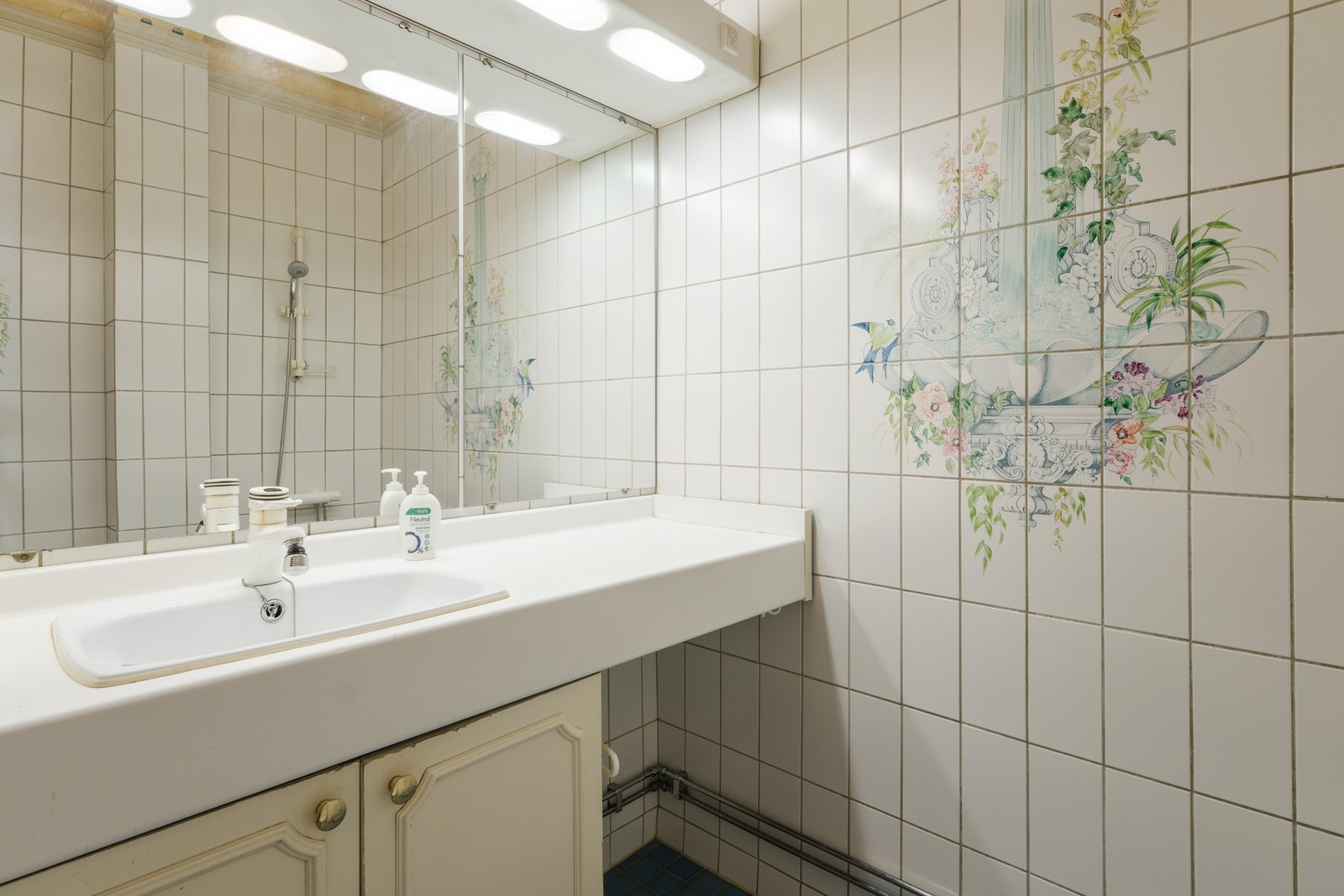 Badet er innredet med vegghengt baderomsinnredning med profilerte lyse fronter og benkeplate av laminat, nedsenket servant, speil, belysning og stikkontakt over servant, dusj med oppkant på gulv, samt toalett. Galleribilde