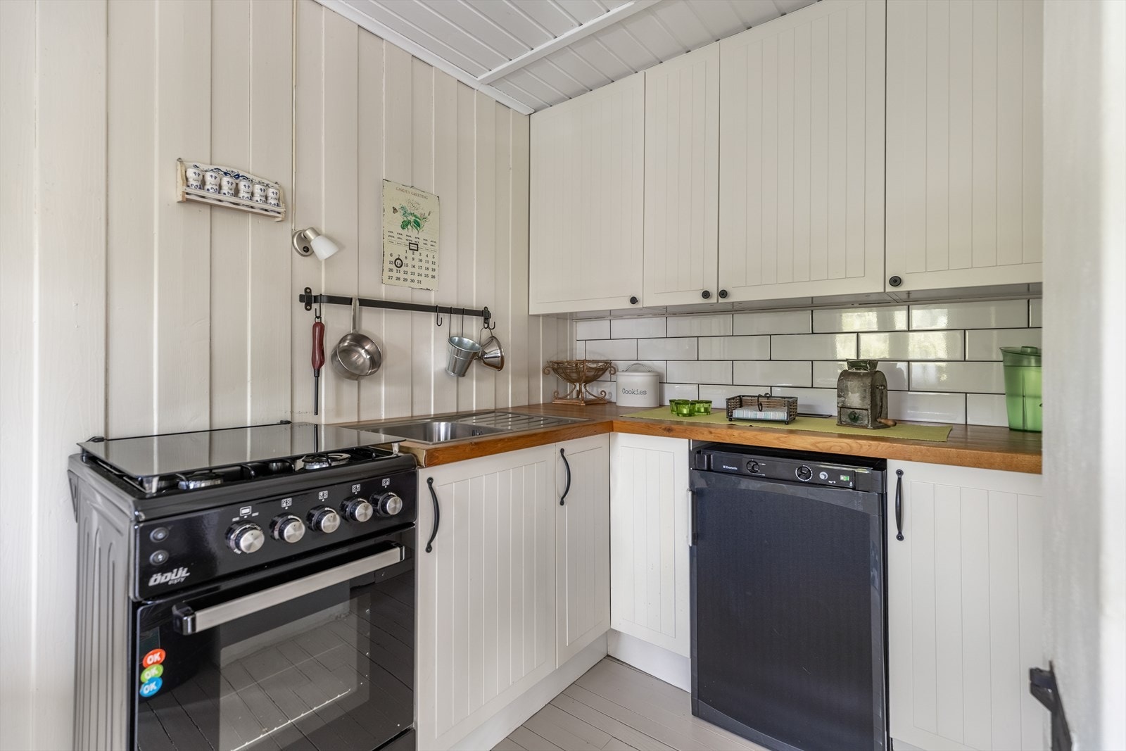 Kjøkkeninnredning med malte fronter og heltre benkeplate. Frittstående hvitevarer og ventilator i skap Galleribilde