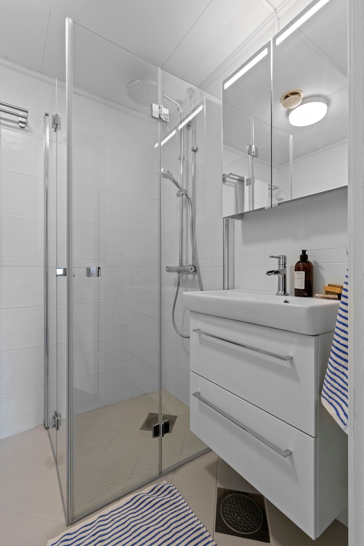 Badet har varmekabler, servant med slette fronter, gulvstående toalett og dusjhjørne med to foldbare glassdører Galleribilde