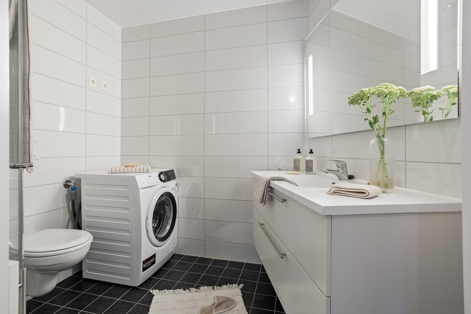 Pent bad som inneholder vegghengt toalett, dusj med vendbare vegger, og servant med skapinnredning. Det er også opplegg for vaskemaskin Galleribilde